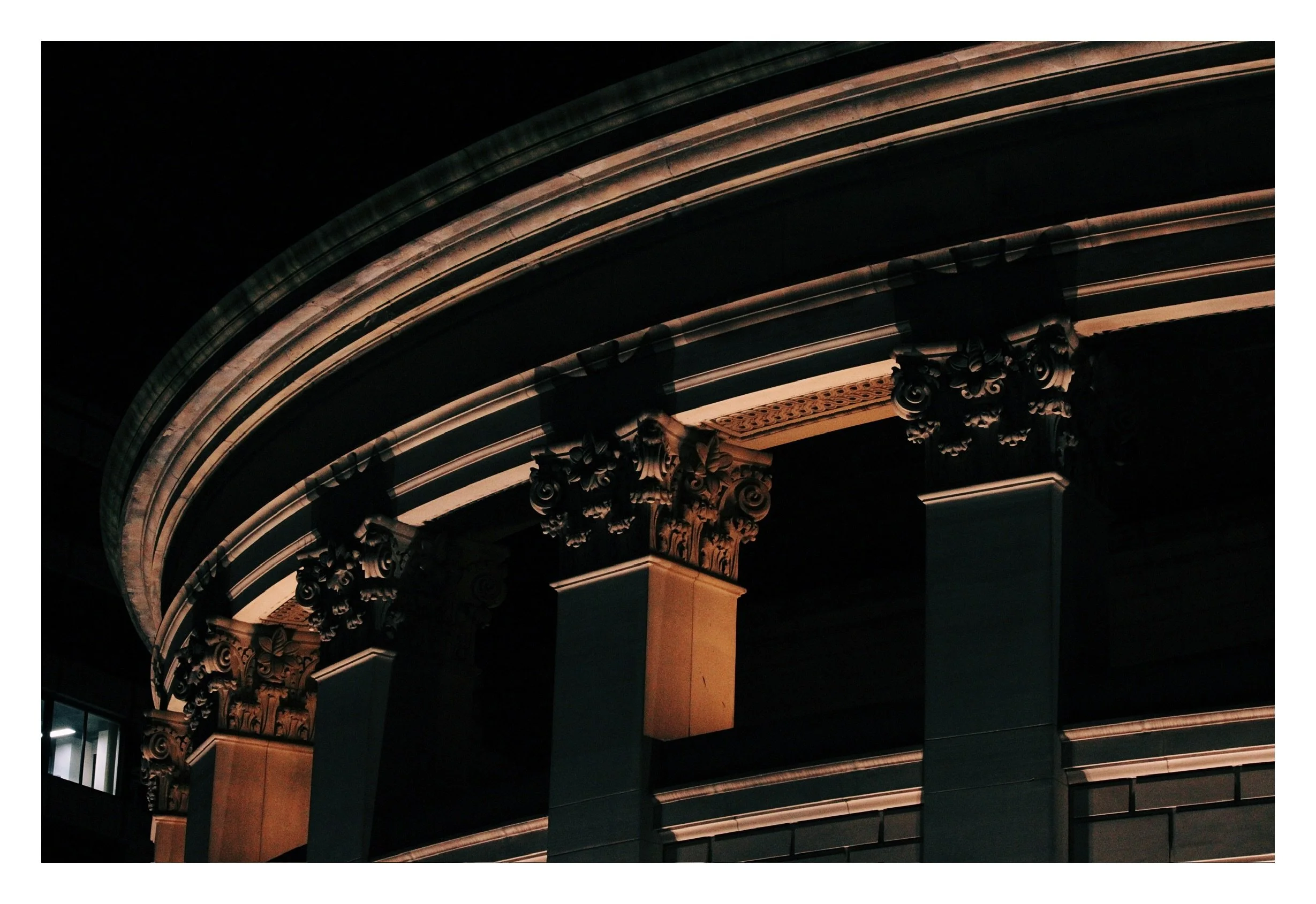 Night view of architectural columns and a curved balcony with ornate details, illuminated in warm lighting.