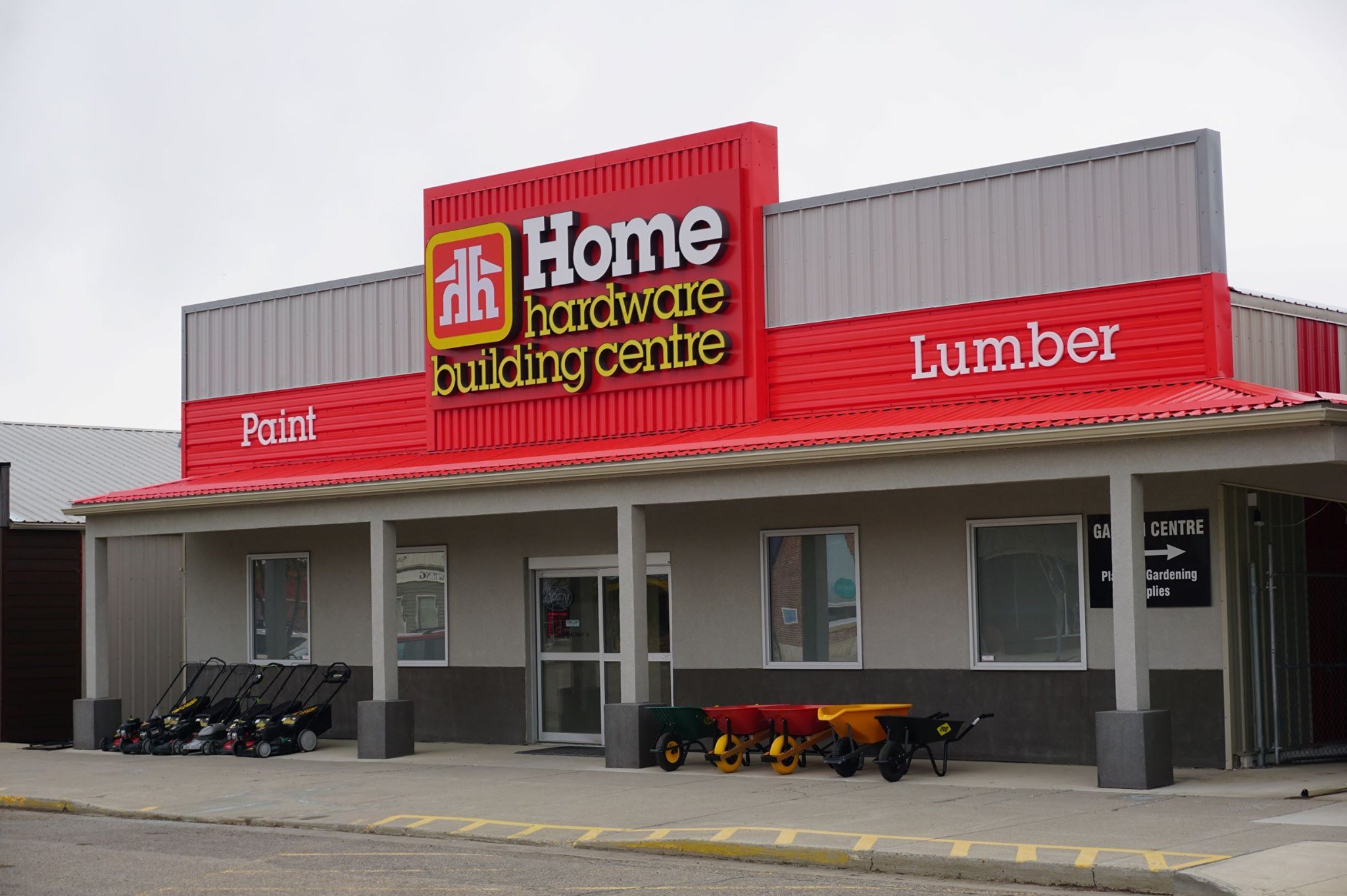 Exterior view of a hardware store named 'Home Hardware Building Centre' with signs indicating paint and lumber sections, and shopping carts outside.