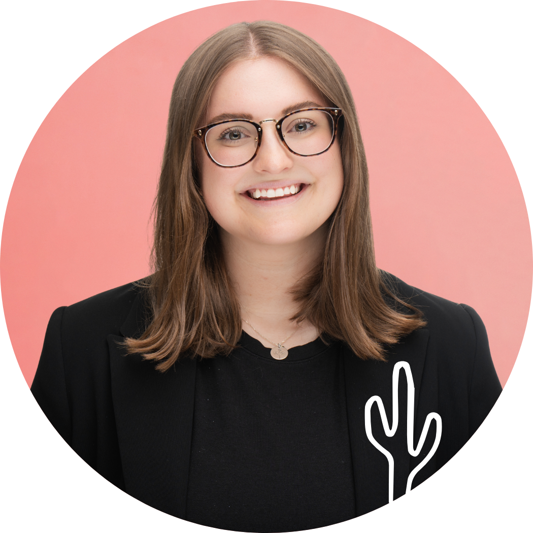 A young woman with shoulder-length brown hair, wearing glasses, a black blazer, and a necklace, smiling against a pink background with a white cactus illustration overlay.
