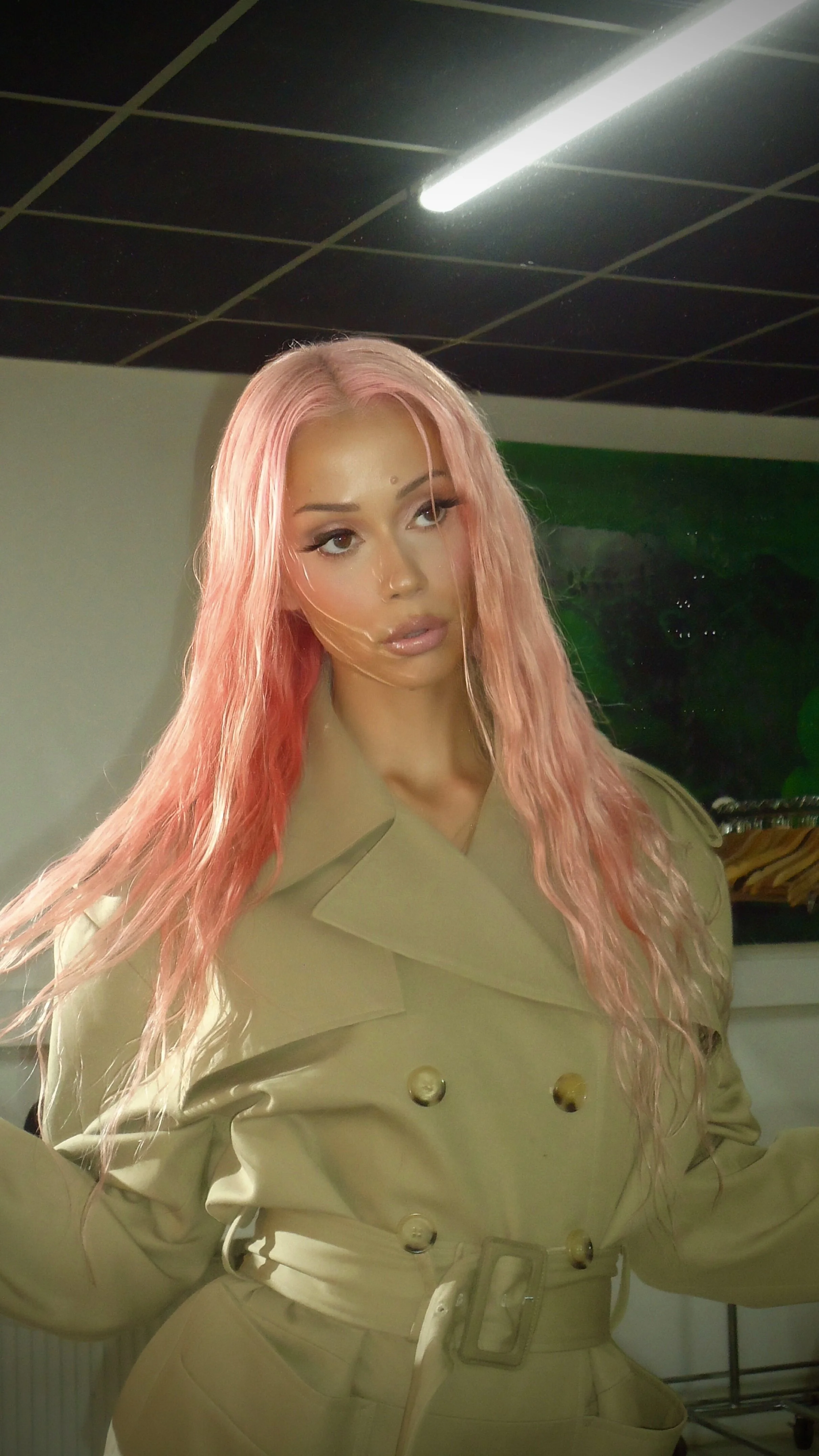A woman with long pink hair wearing a beige trench coat with gold buttons.