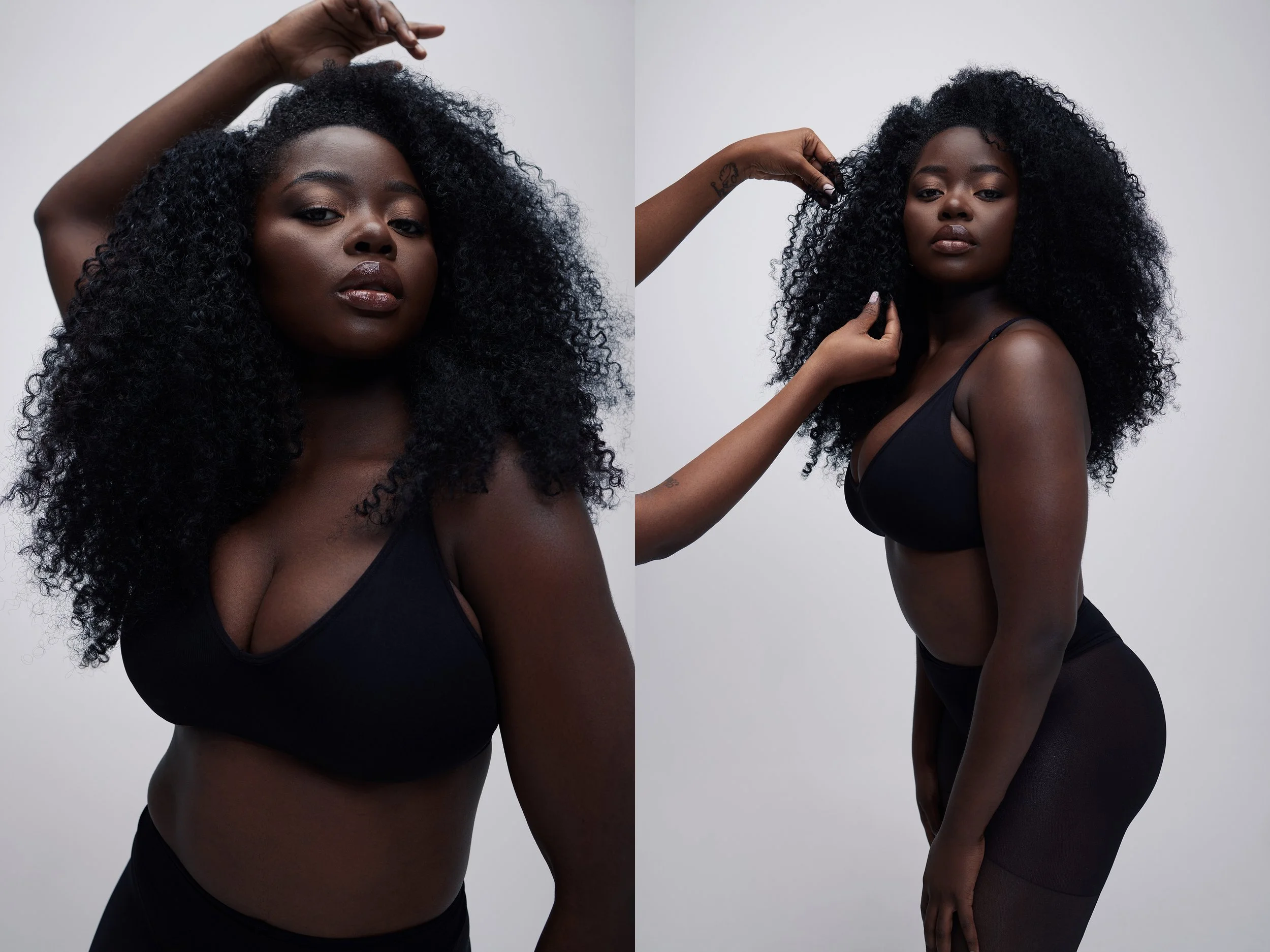 A young Black woman with voluminous curly hair posing in a black sports bra and black shorts against a plain light gray background.