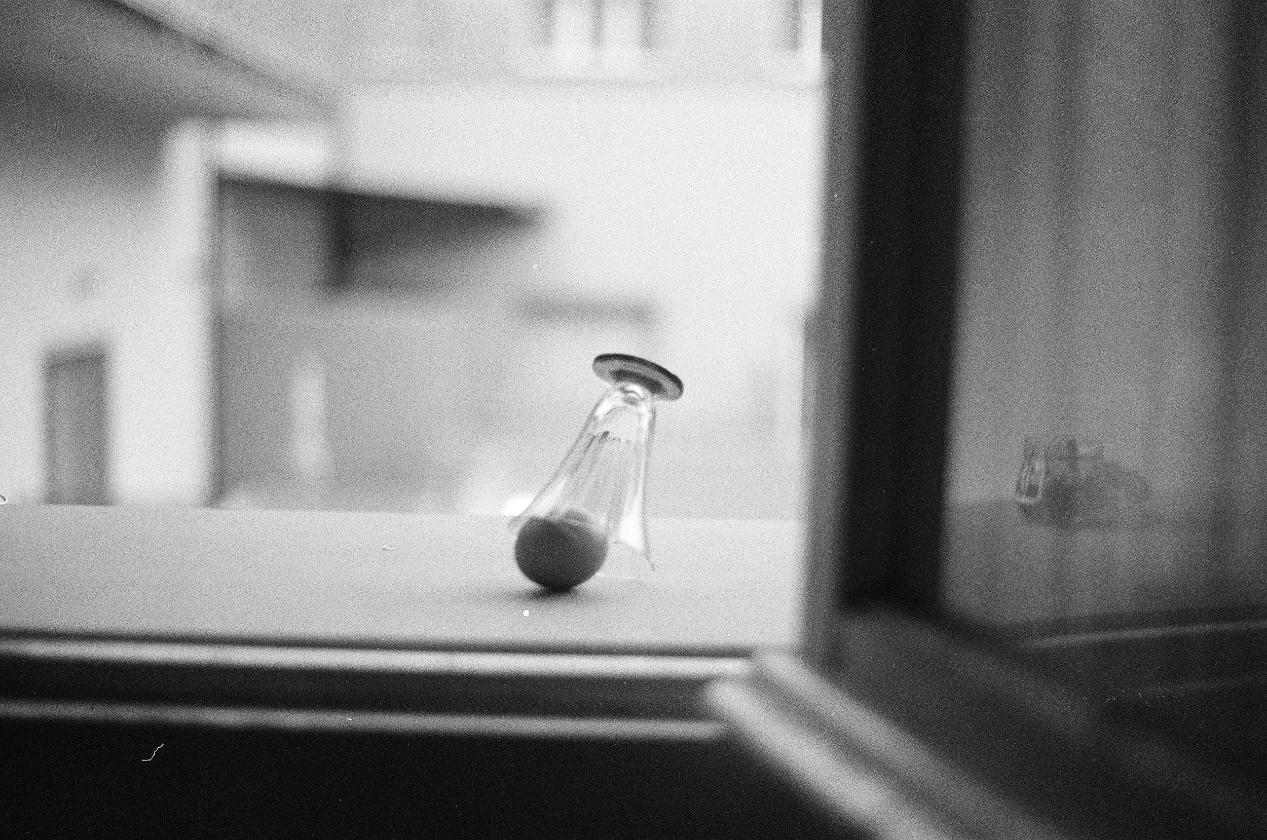 Un becher di vetro con un tappo in cima, appoggiato su una superficie e leggermente inclinato, visibile attraverso una finestra o uno scomparto di frigorifero.