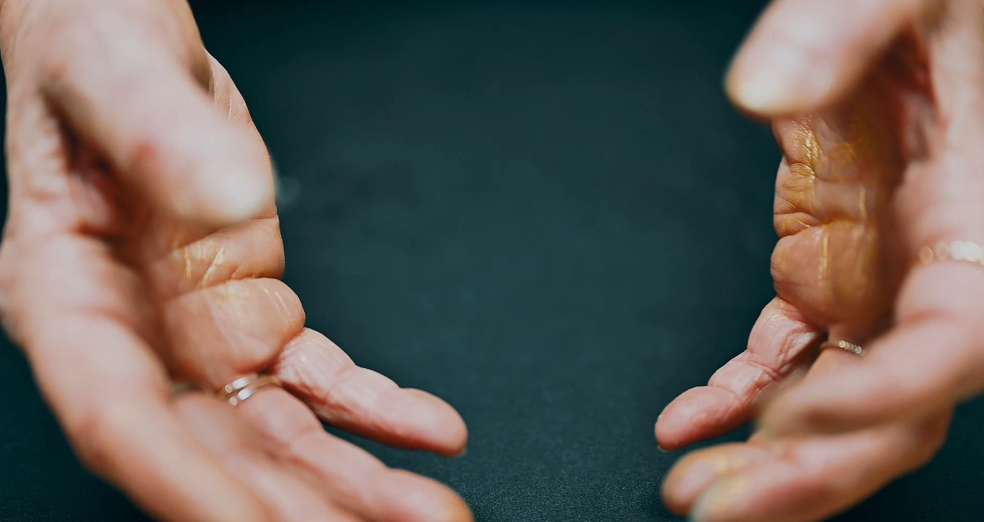 Le mani di una persona con alcune anelli sul dito, con il palmo rivolto verso l'alto, si trovano sopra una superficie scura