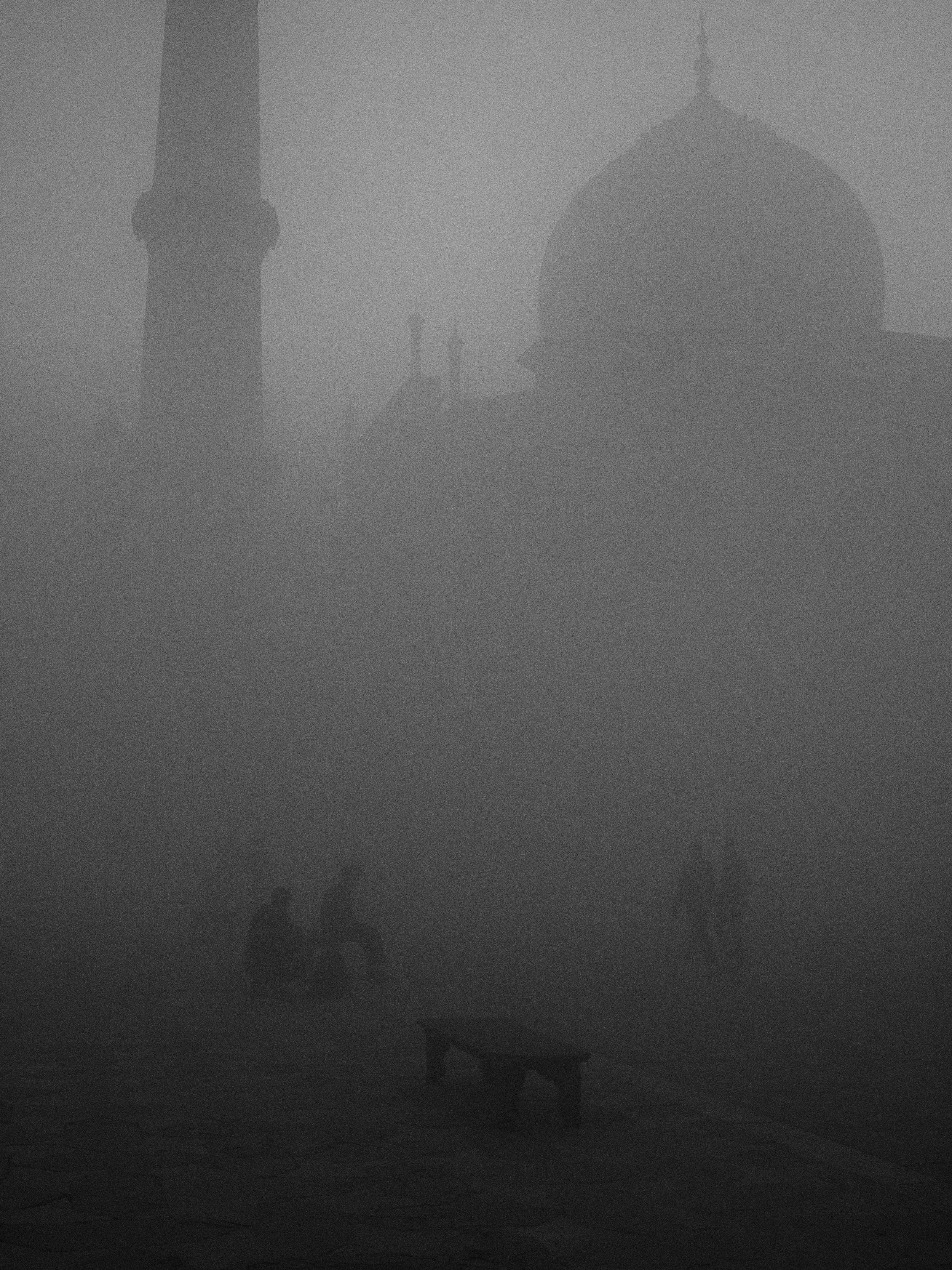 Silhouette di persone e monumenti, tra cui un grande edificio con una cupola e una torre, visibili attraverso una fitta nebbia.