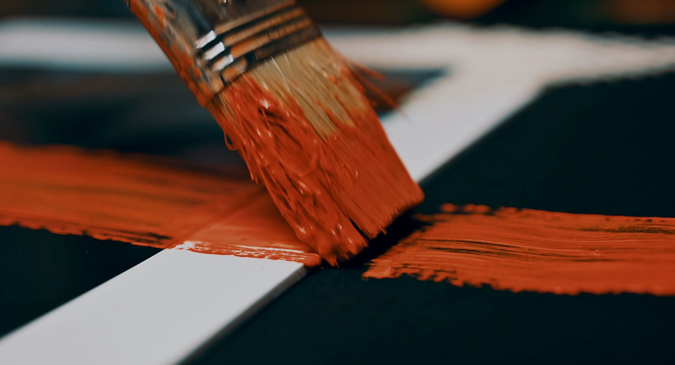 Pennello di vernice che sta dipingendo una linea bianca su una superficie nera.