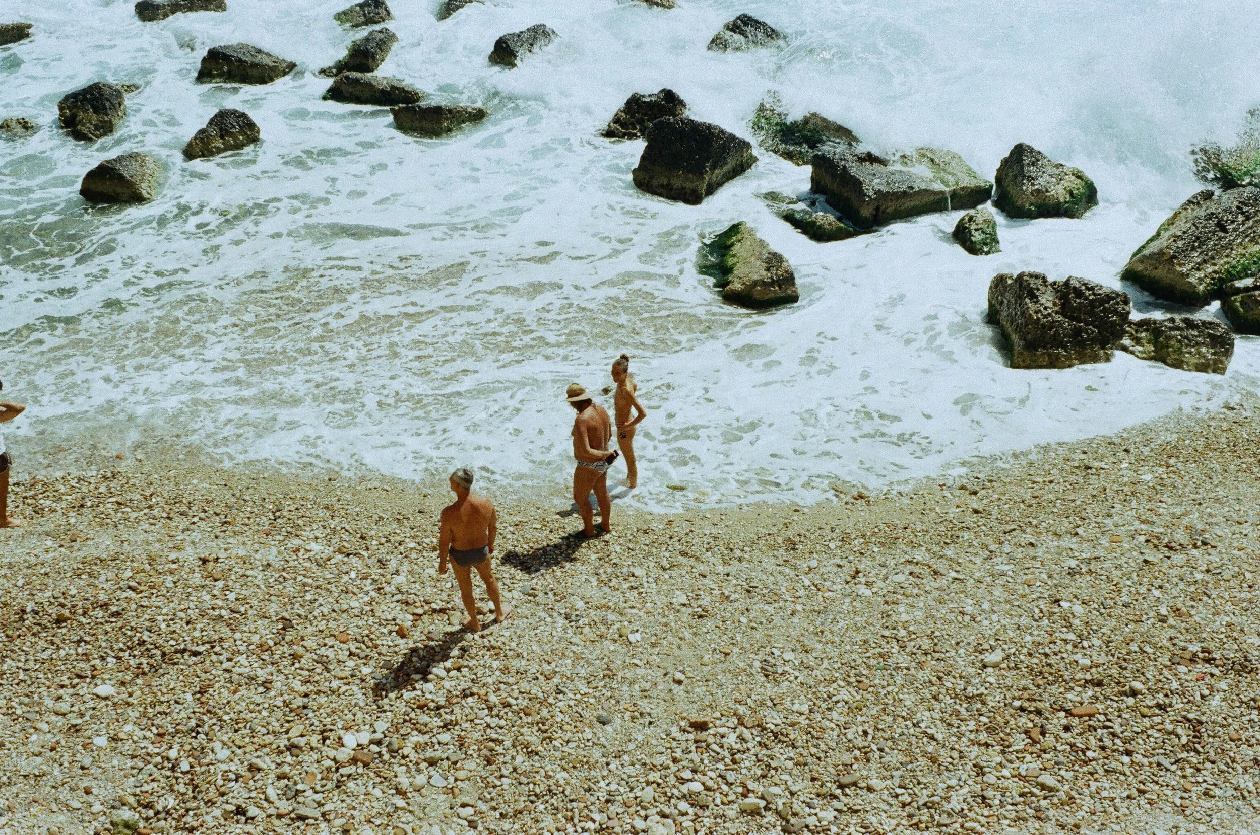 Spiaggia con persone che passeggiano vicino al mare con onde e pietre.