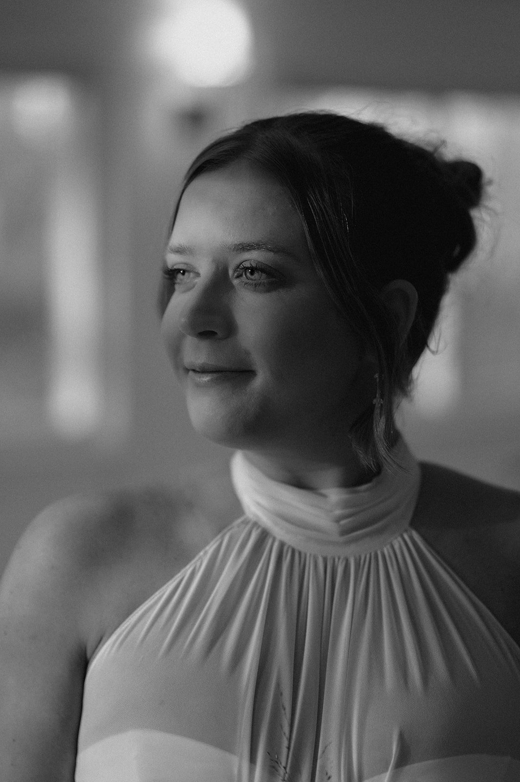 Black and white portrait of a woman with hair in an updo, wearing a pleated high-neck dress, looking to the side with a gentle expression.