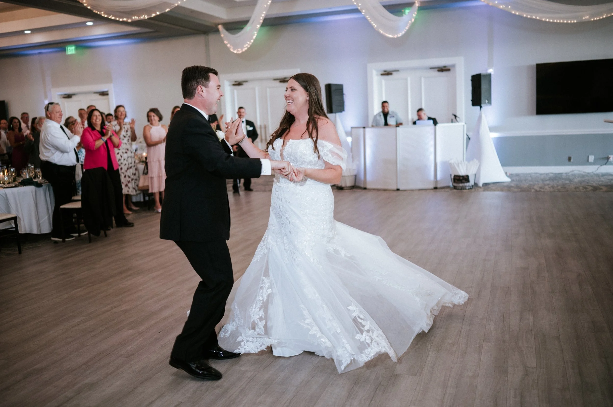 A bride and groom dancing at their wedding reception with guests watching and clapping in the background.