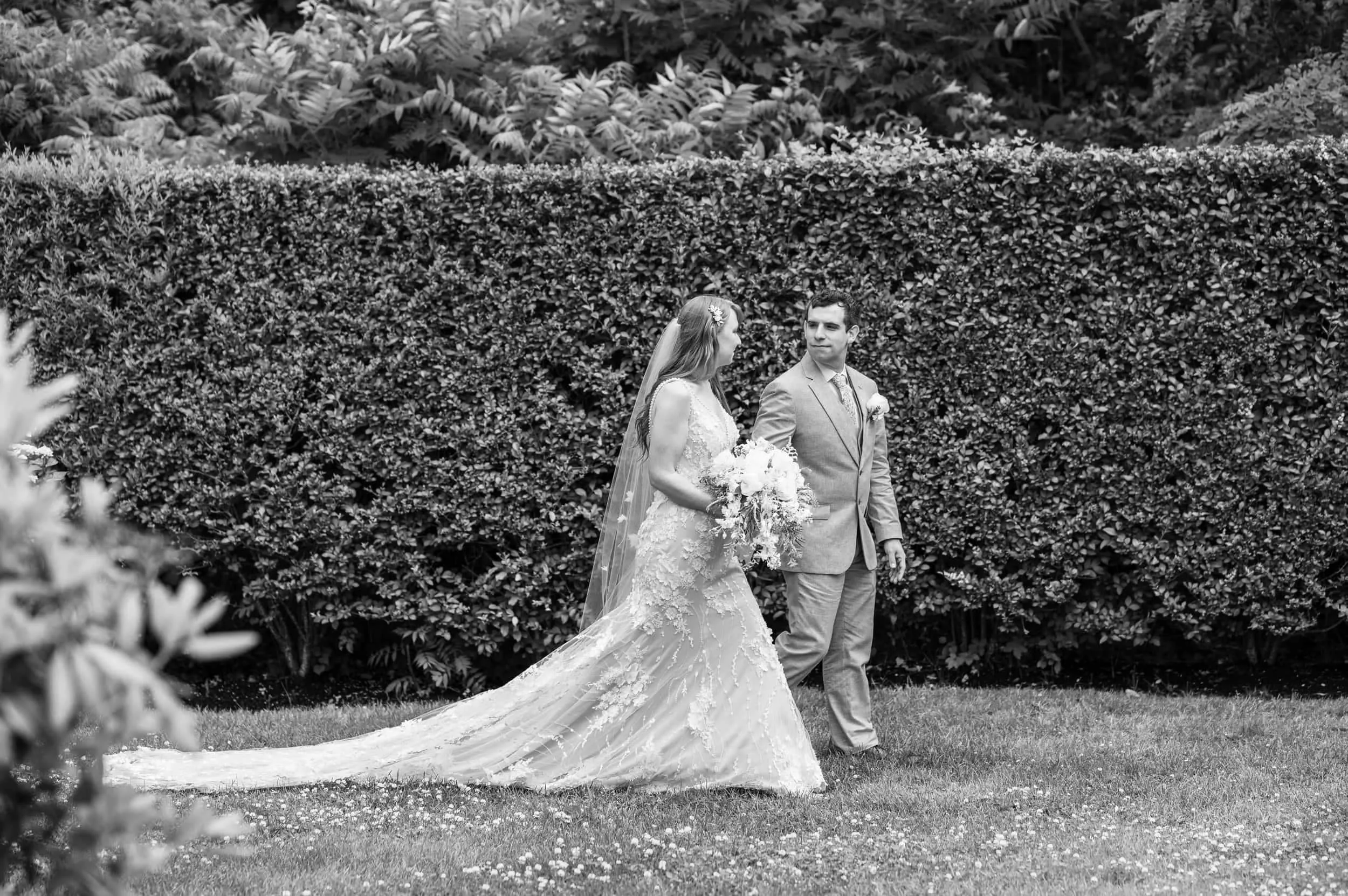 Black and white photo of a couple during their elopement walking while holding hands through the garden at the Sagamore in Bourne, MA