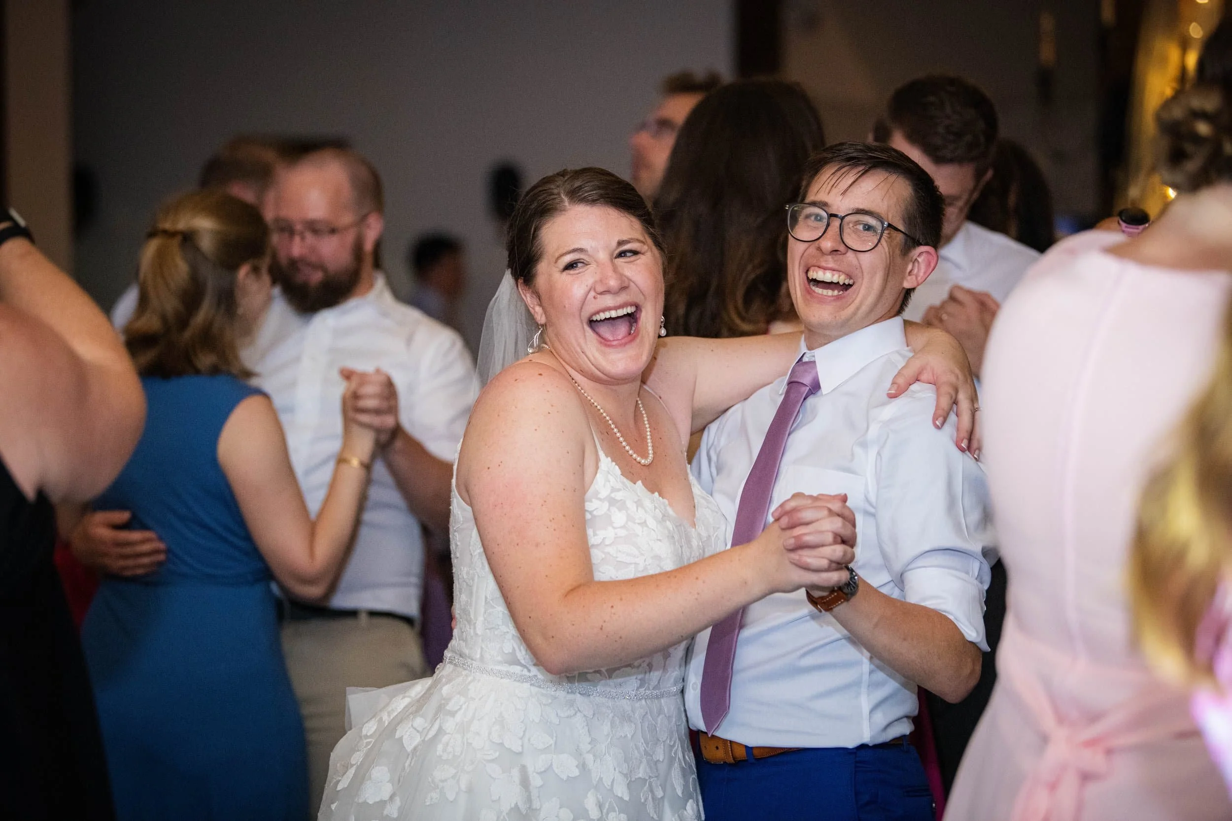 A bride and groom dancing happily at their wedding reception surrounded by friends.