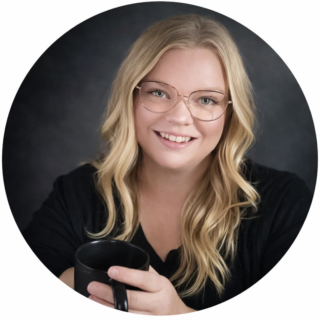 A smiling woman with long blonde hair, glasses, and a black shirt holding a black mug, against a dark background.