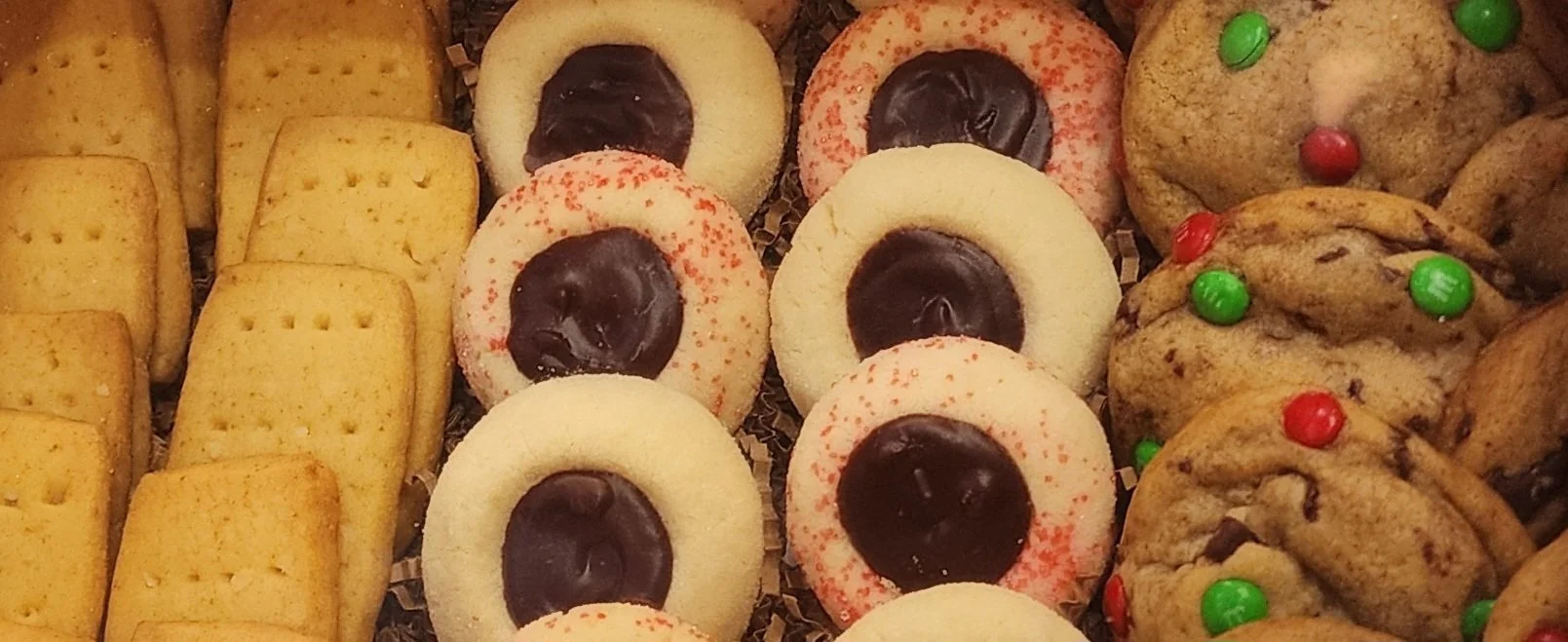 Assorted cookies with different shapes and toppings, including rectangular butter cookies, round sandwich cookies with chocolate centers, and large cookies with colorful candy pieces.