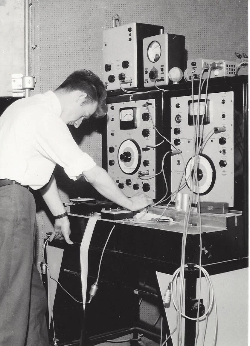 A man working with vintage electronic testing and measurement equipment in a laboratory setting.