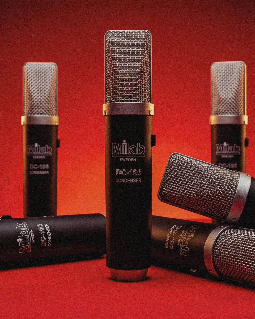 Five vintage-style microphones with black bodies and silver grilles, branded Milab from Sweden, arranged on a red background.