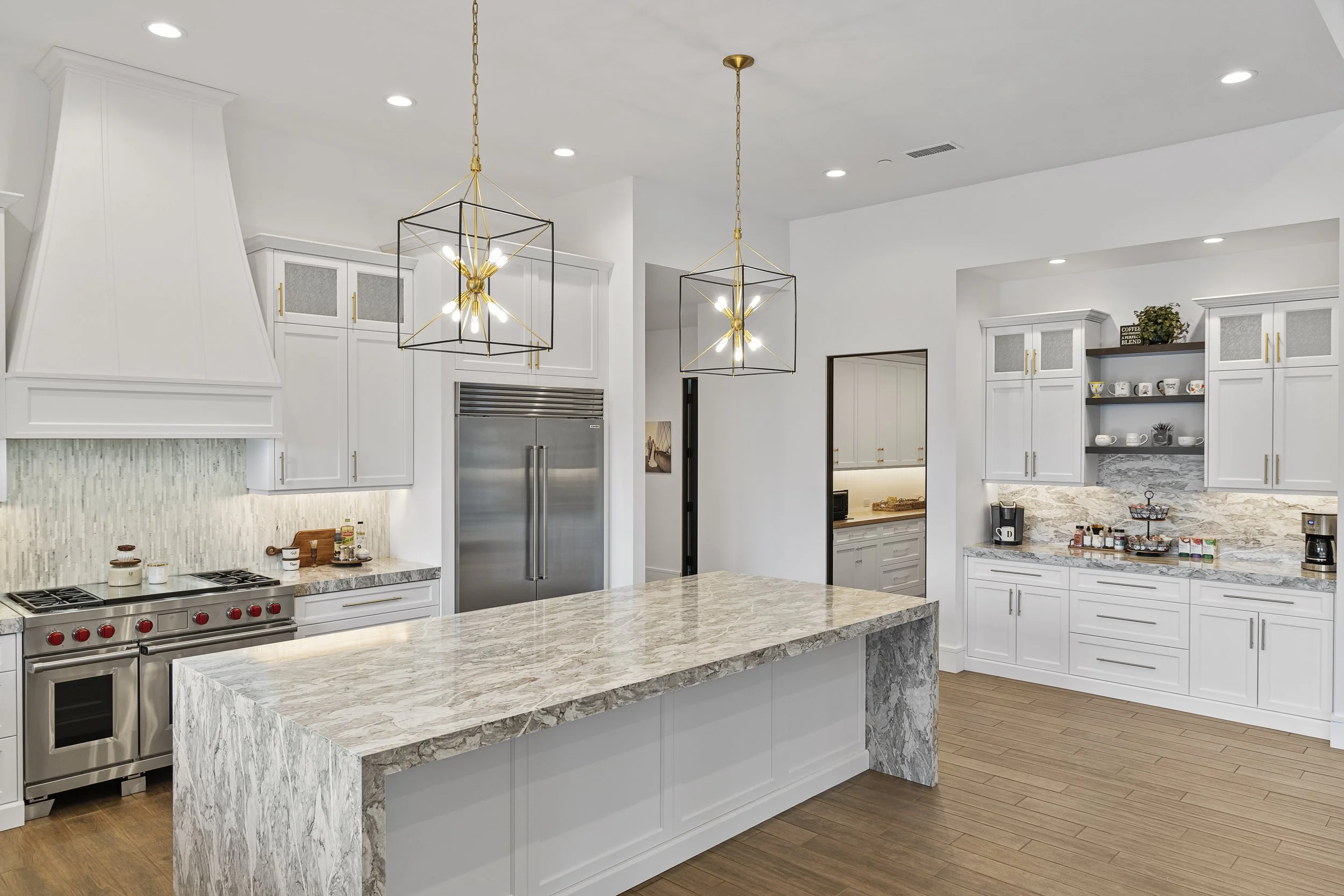 Modern white kitchen with marble countertops, stainless steel appliances, and pendant lights.