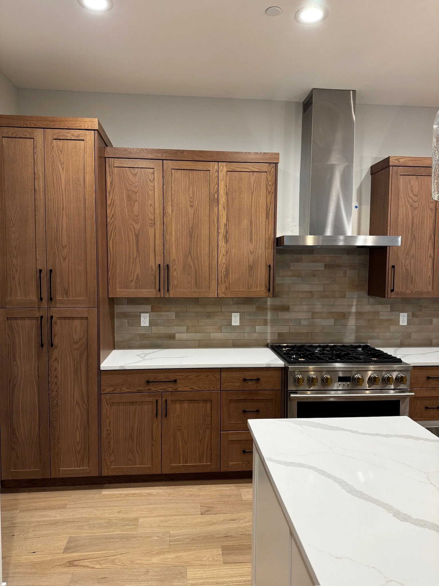 Kitchen with wooden cabinets, marble countertops, a stainless steel range and hood, and a beige brick backsplash.