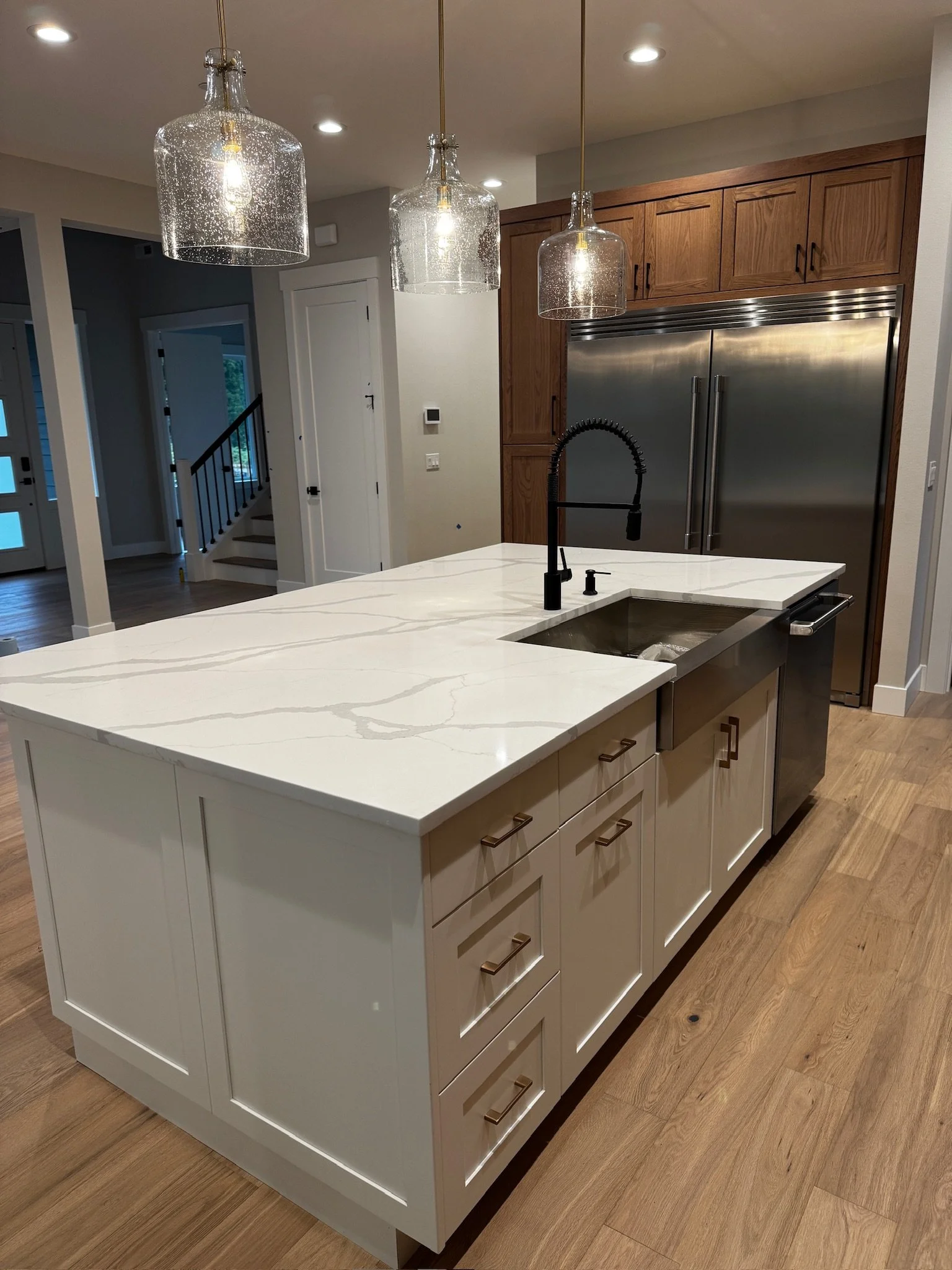 Modern kitchen island with white marble countertop, black faucet, and cream cabinet drawers, illuminated by three hanging glass pendant lights.