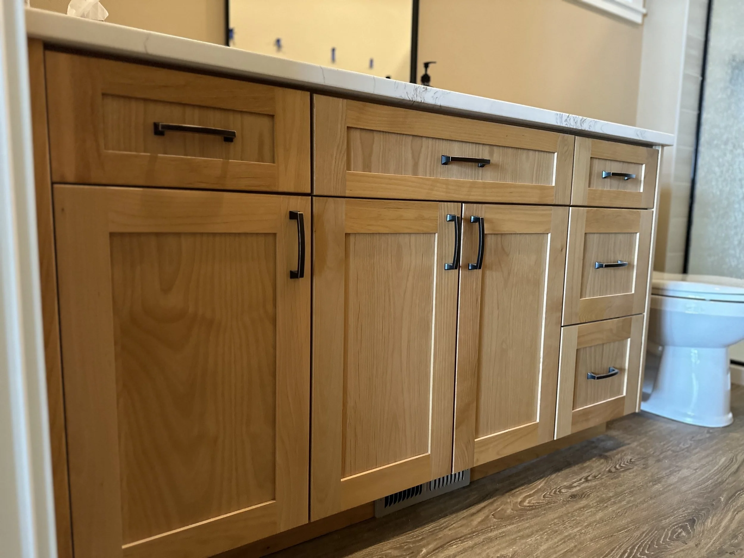 A bathroom vanity with multiple wooden cabinets and drawers, a marble countertop, and a mirror above it. To the right, part of a white toilet is visible.