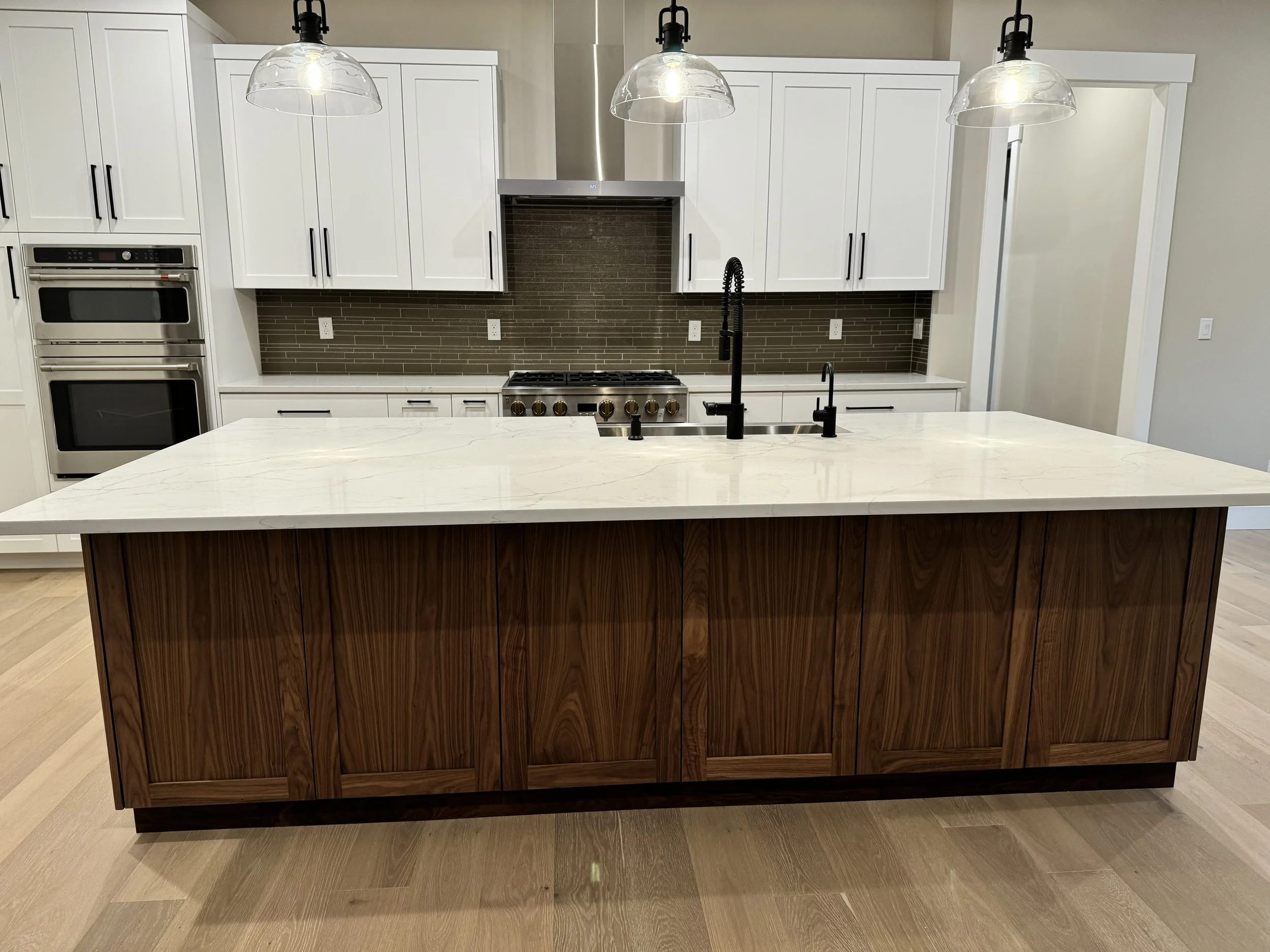 Modern kitchen with a large island featuring a white marble countertop and wooden base, white cabinets, stainless steel appliances, and three hanging glass pendant lights.
