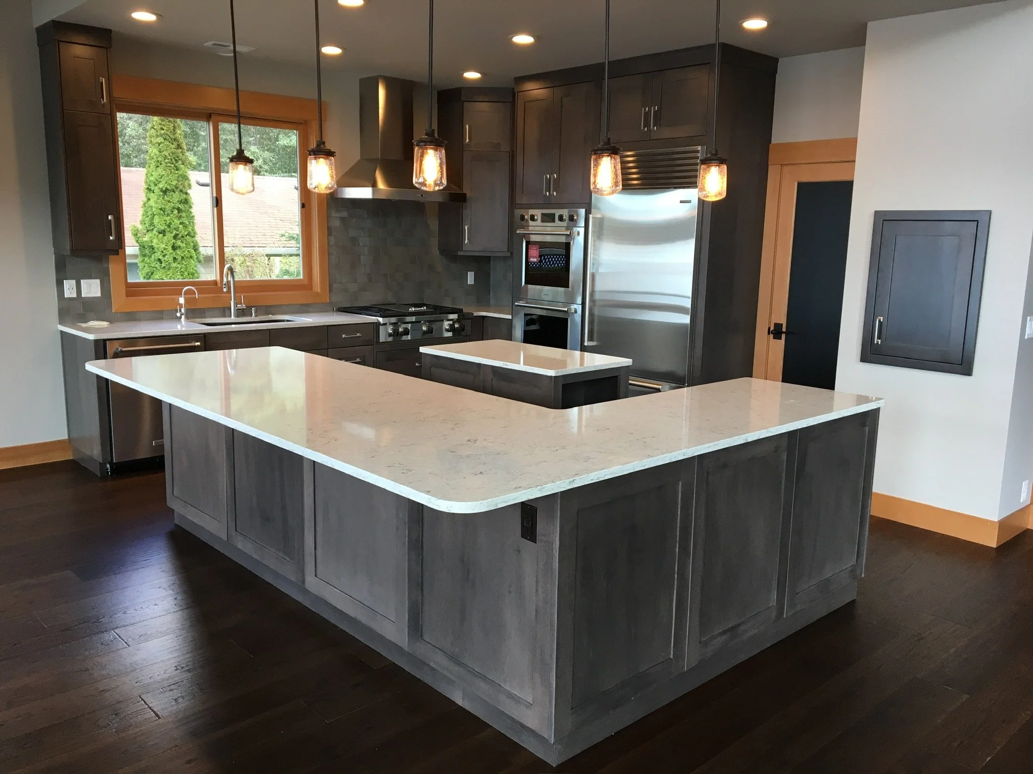 Modern kitchen with dark wood cabinets, a white marble island, stainless steel appliances, and pendant lighting.