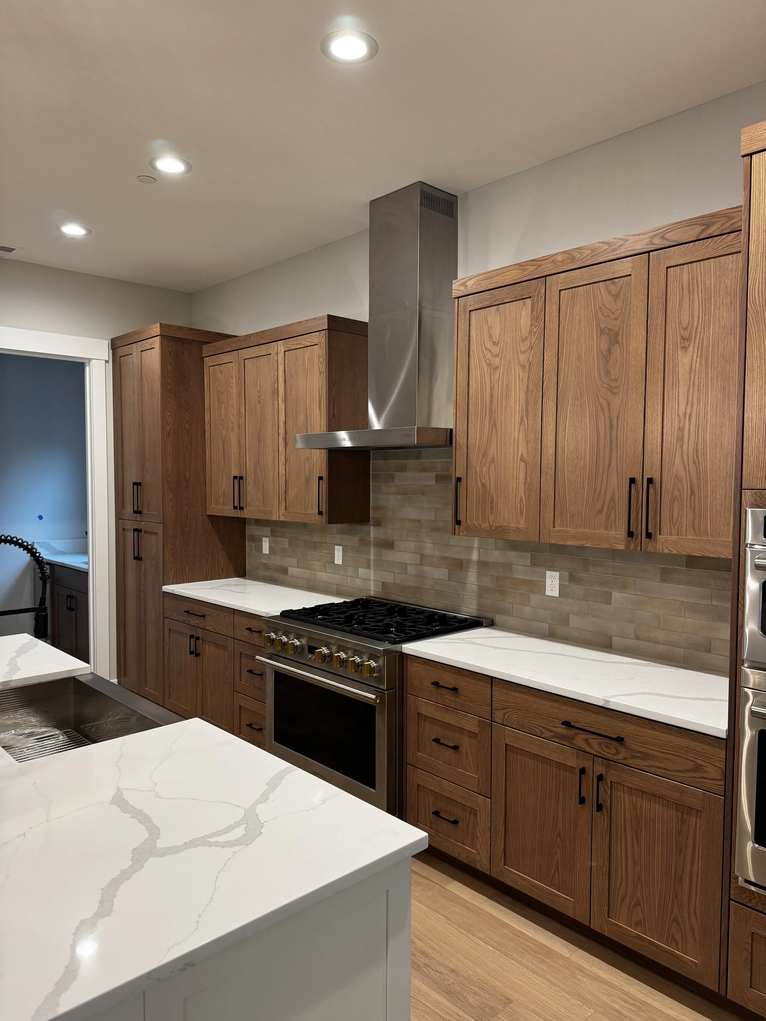 Modern kitchen with wooden cabinets, white marble countertops, stainless steel oven, and beige tile backsplash.
