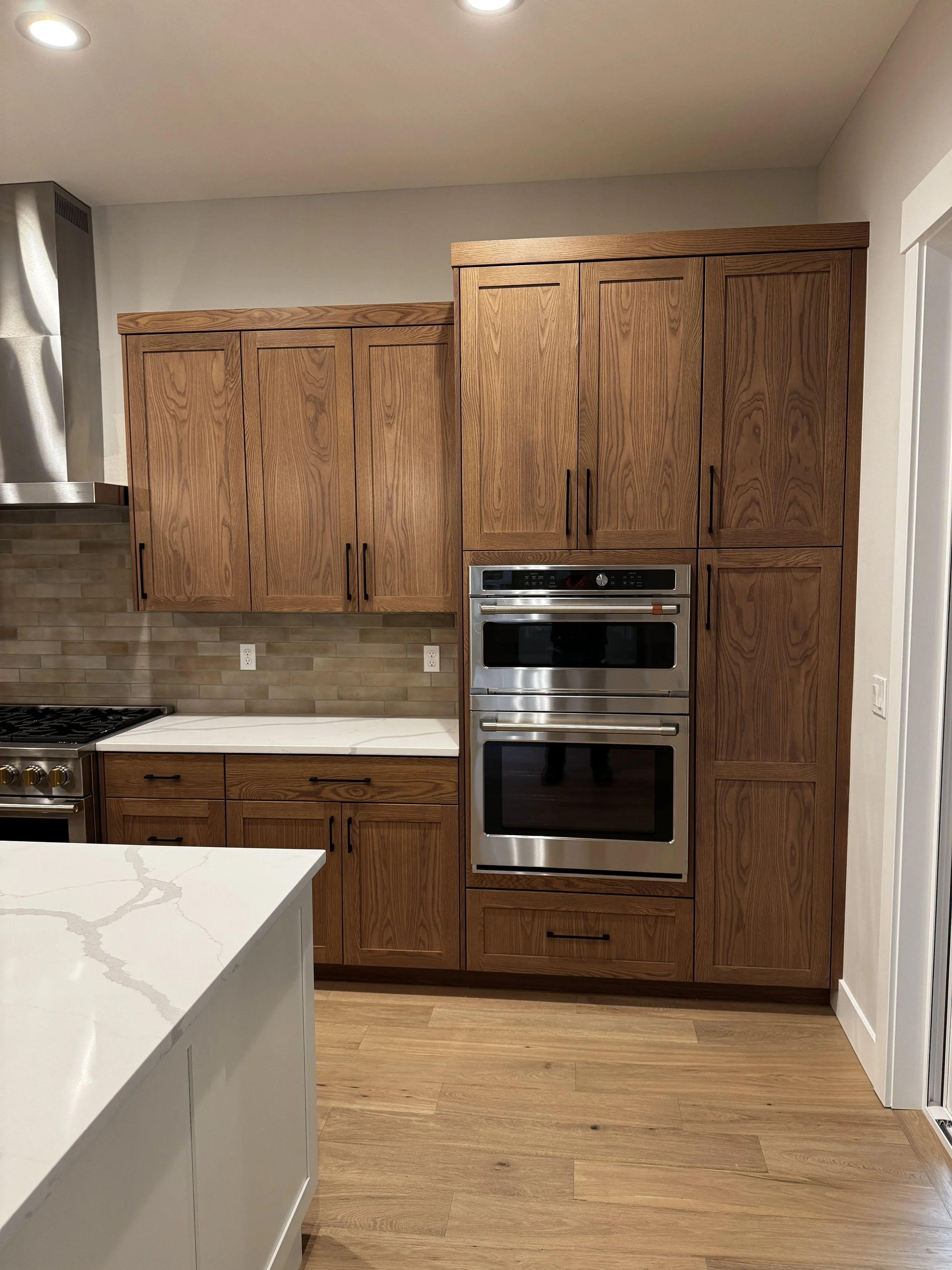Kitchen with wooden cabinets, stainless steel double oven, marble countertop, and beige tile backsplash.