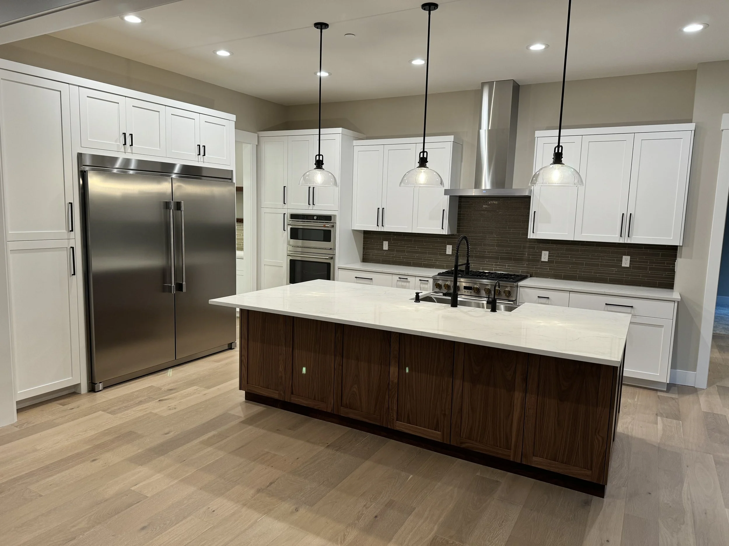 Modern kitchen with white cabinets, stainless steel appliances, and a large island with a white marble countertop, pendant lights, and a brown tiled backsplash.