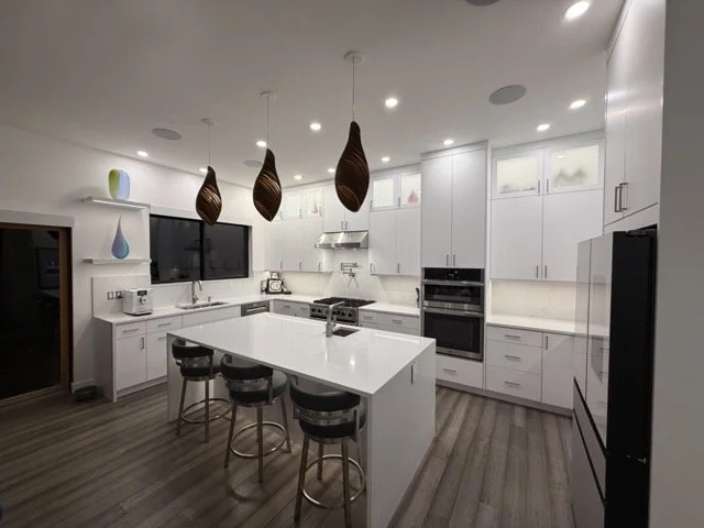 Modern kitchen with white cabinets, an island with three black bar stools, pendant lights, and stainless steel appliances.
