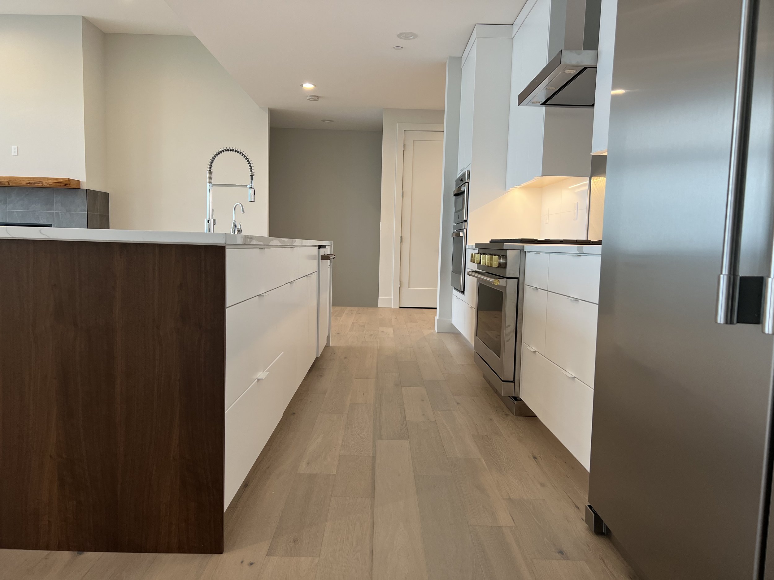 Modern kitchen with white cabinets, stainless steel appliances, a wooden island, and light hardwood floors.