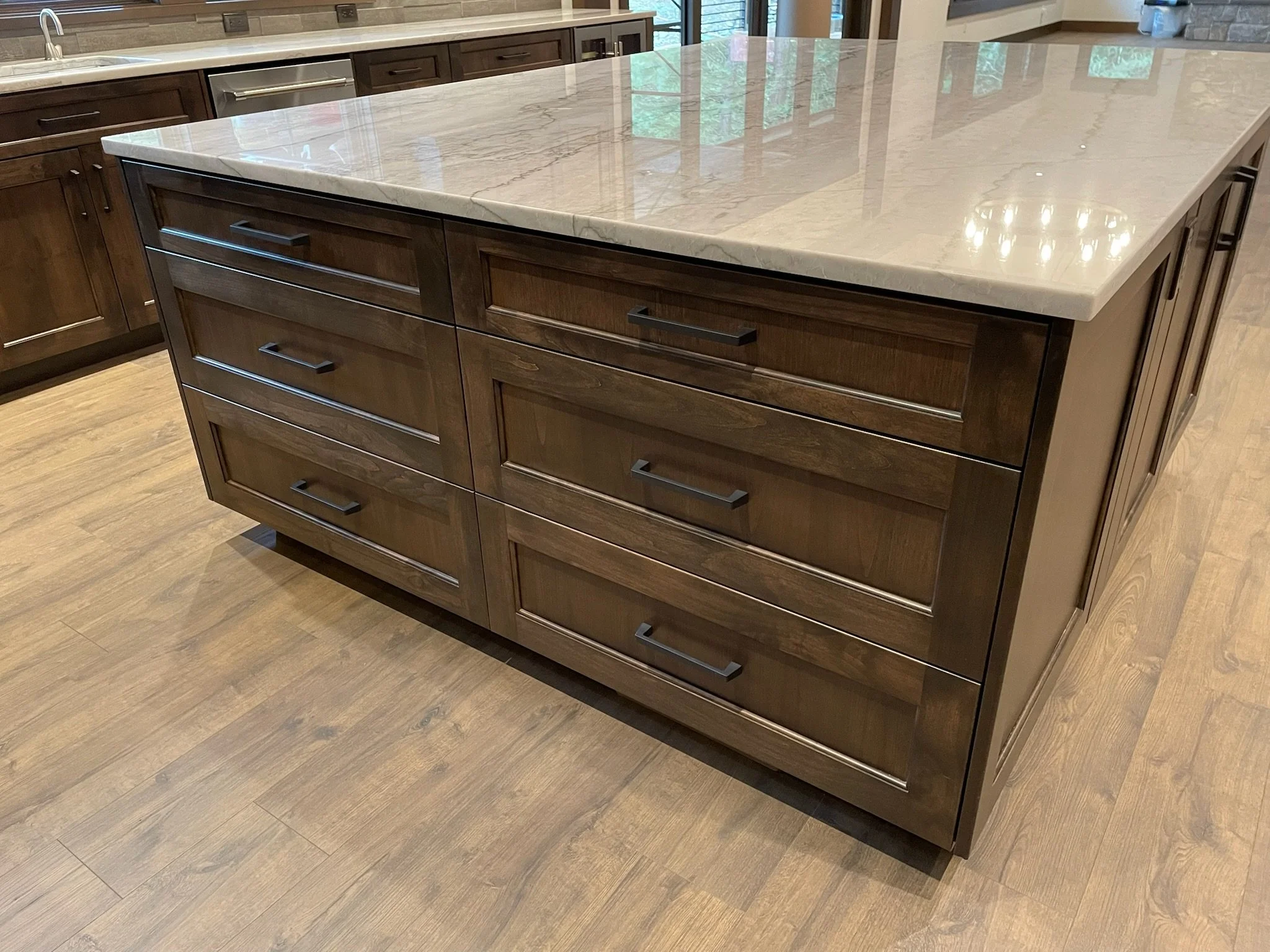 A kitchen island with a white marble top and dark wood drawers with black handles, situated on a wooden floor.