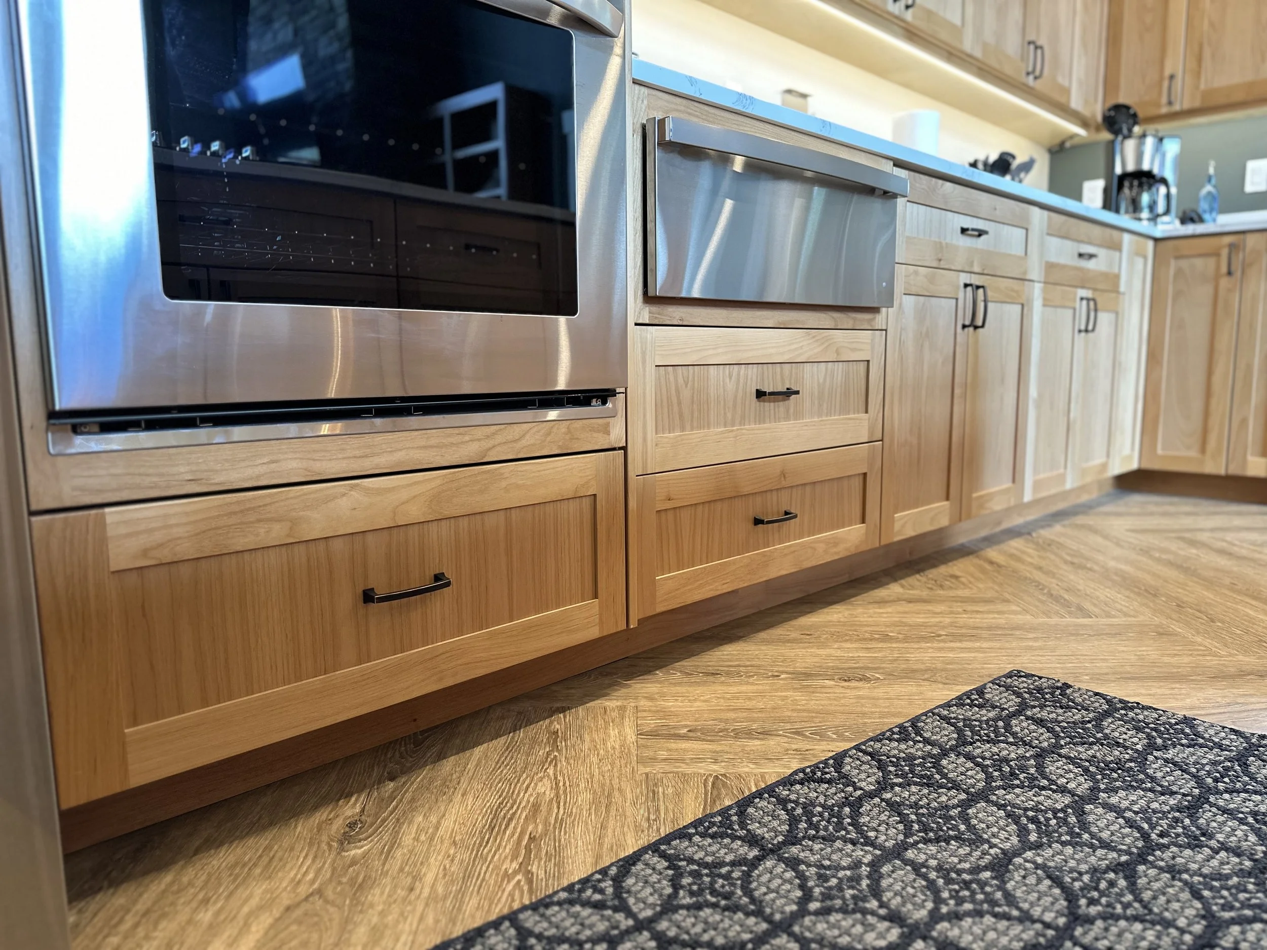 Kitchen with wooden cabinets, a black stovetop oven, stainless steel drawer, and hardwood flooring.