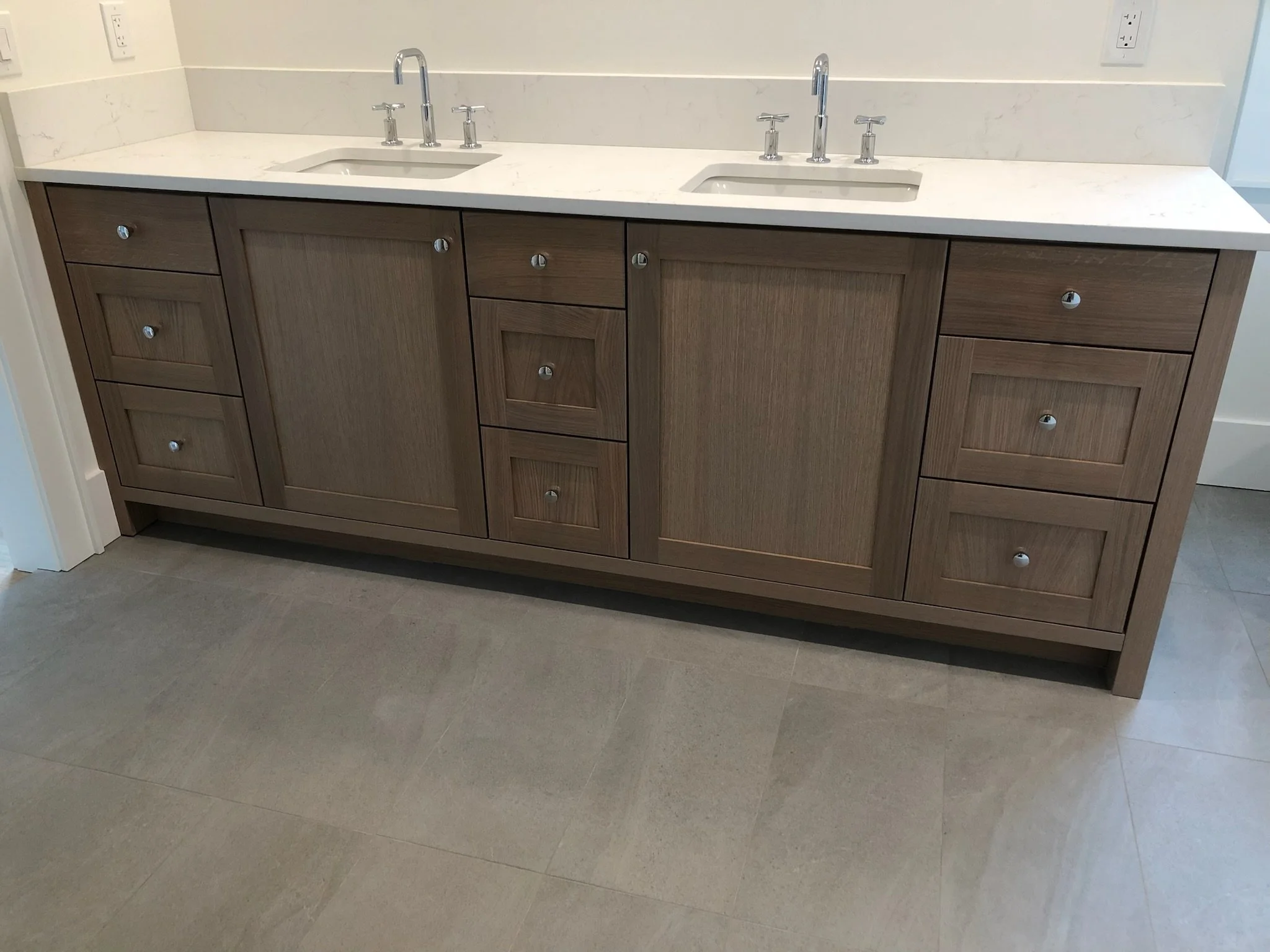 Wooden bathroom vanity with two sinks, marble countertop, and multiple drawers and cabinets.