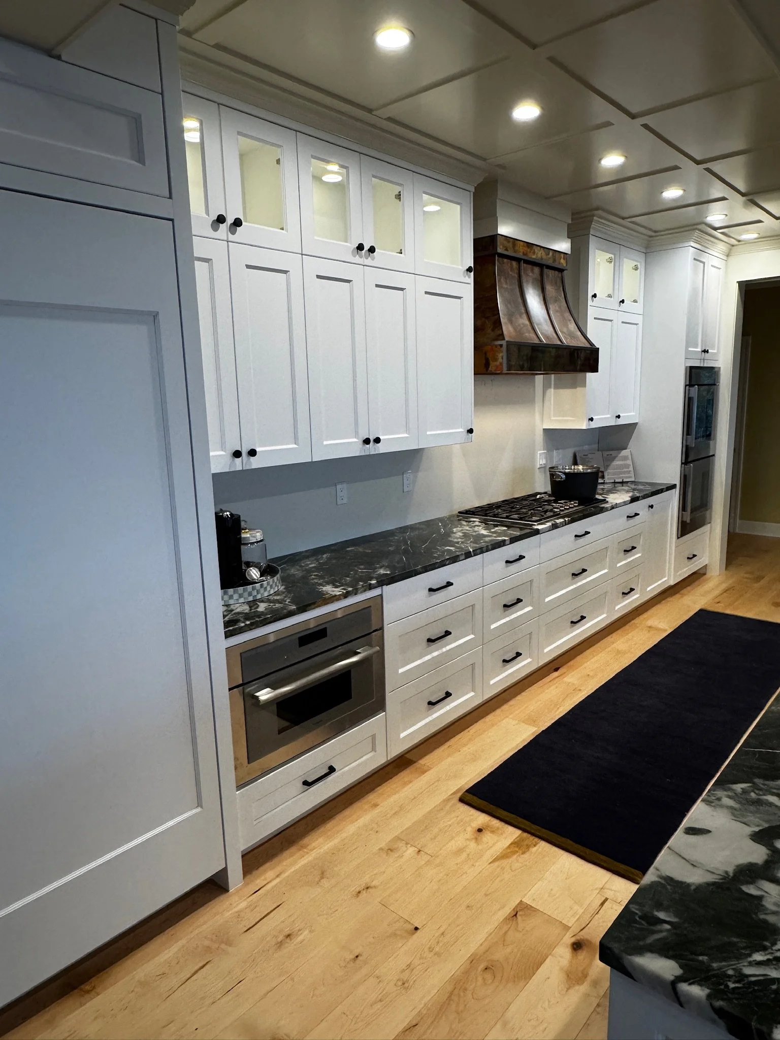 Modern kitchen with white cabinets, black knobs, black marble countertops, a black rug, and built-in appliances.