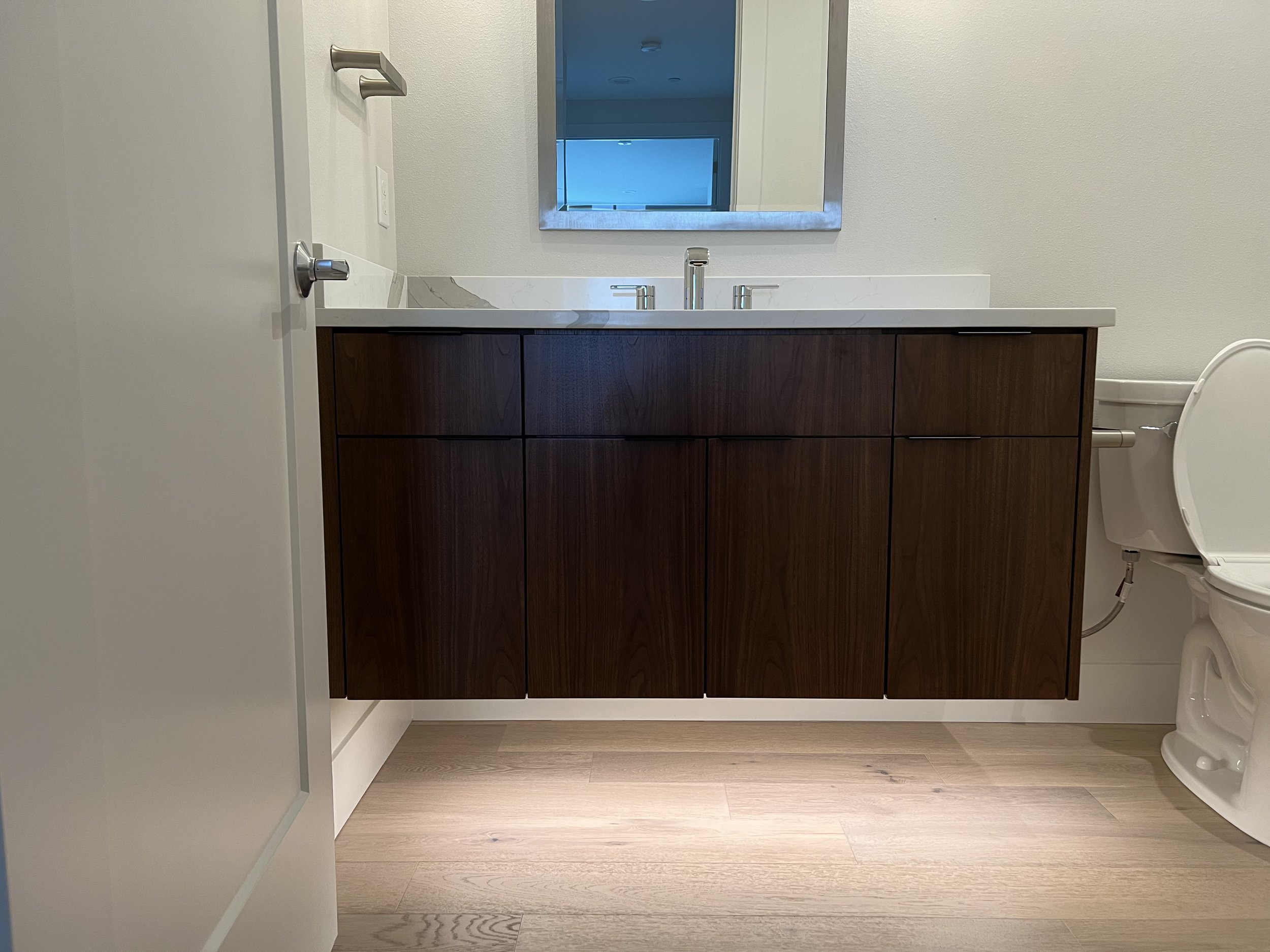 Bathroom with dark wood vanity, white countertop, mirror, faucet, and partially visible toilet