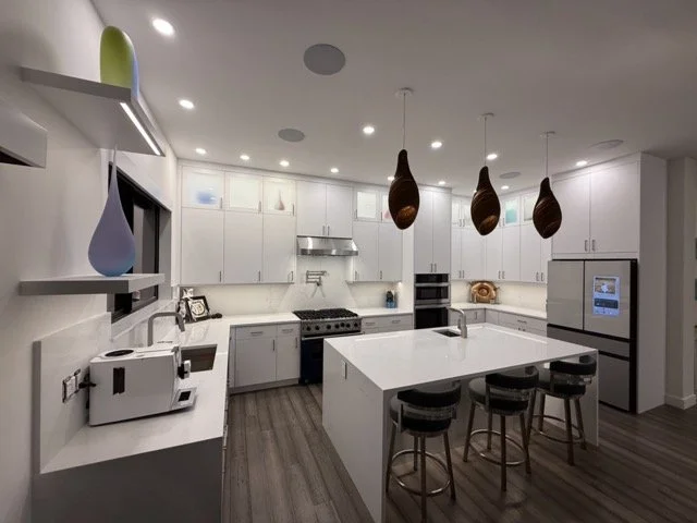 Modern kitchen with white cabinets, a large island with seating, pendant lights, and stainless steel appliances.