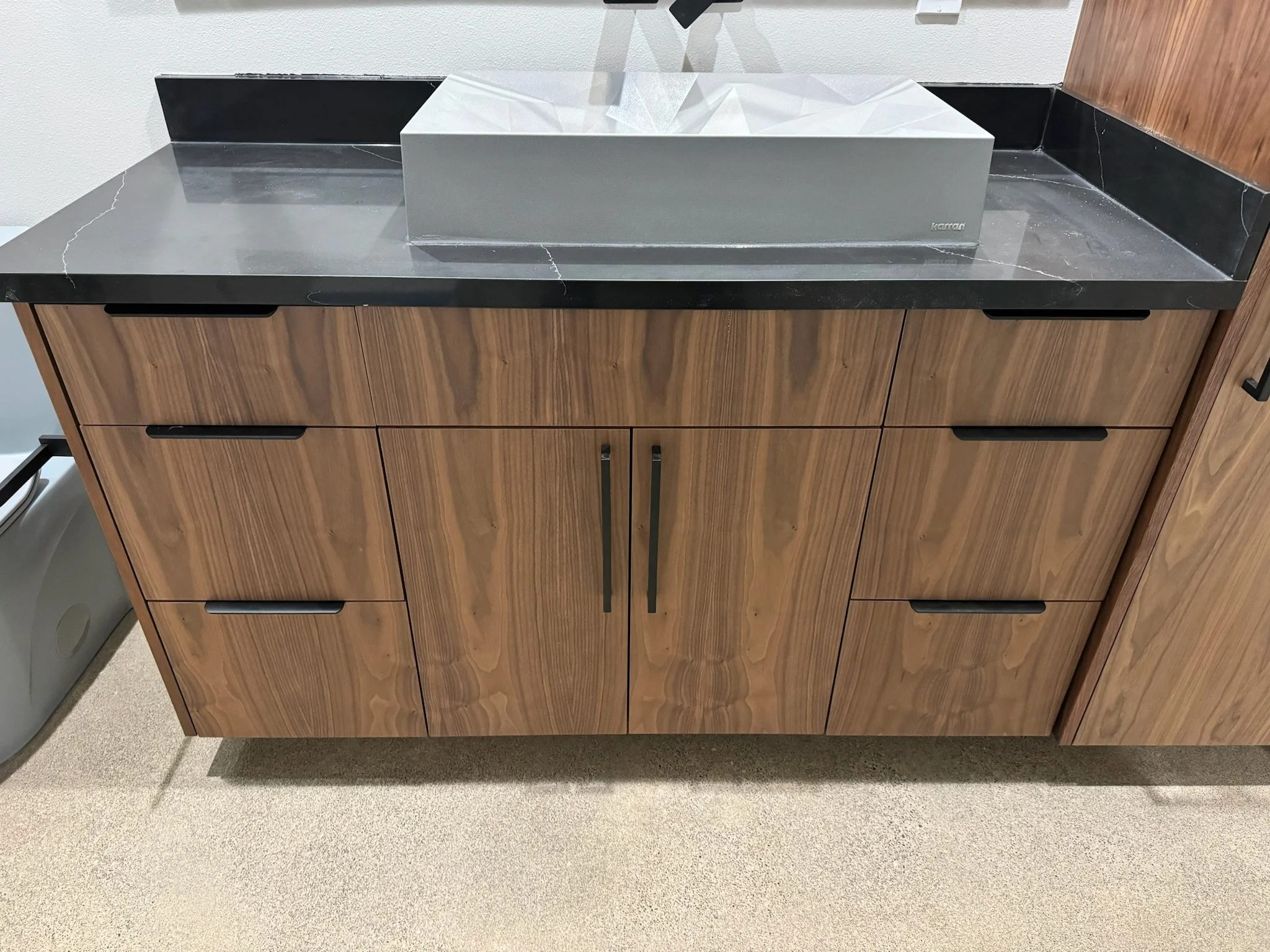 A wooden cabinet with black handles and a black countertop, featuring a tissue box on top.