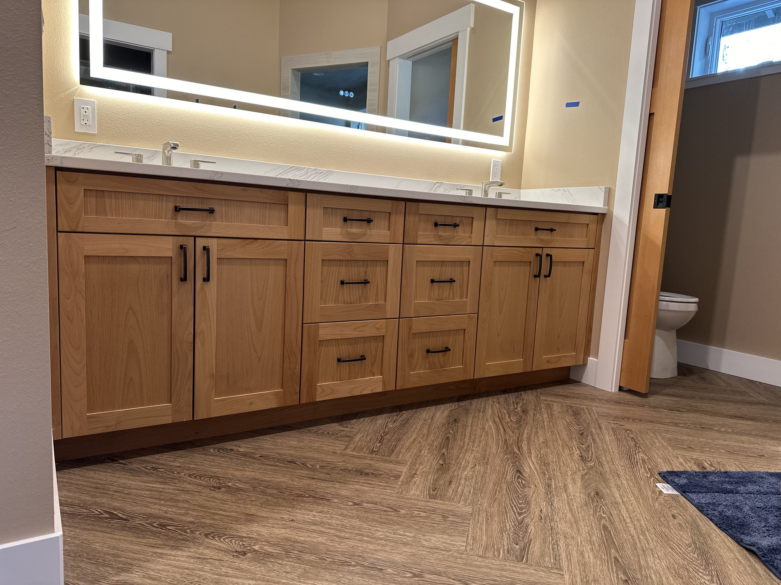 Bathroom vanity with wooden cabinets, marble countertop, and backlit mirror; partially visible toilet and window.