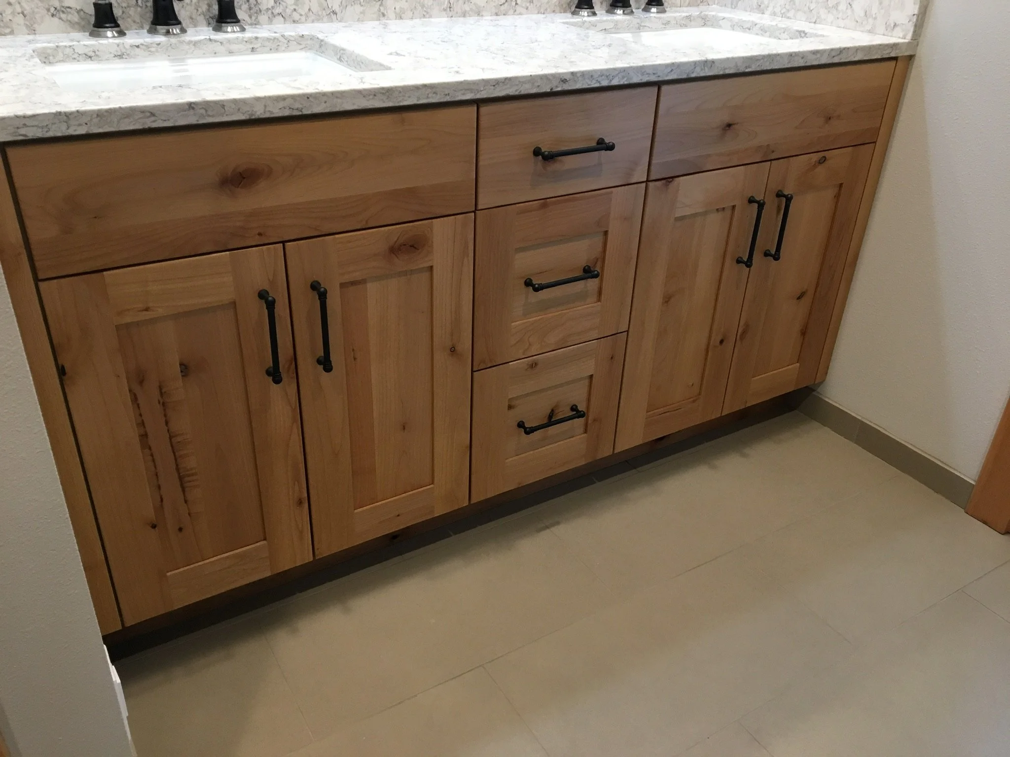 Wooden bathroom vanity with six cabinet doors and three drawers, topped with a granite countertop and black handles, on a tiled floor.