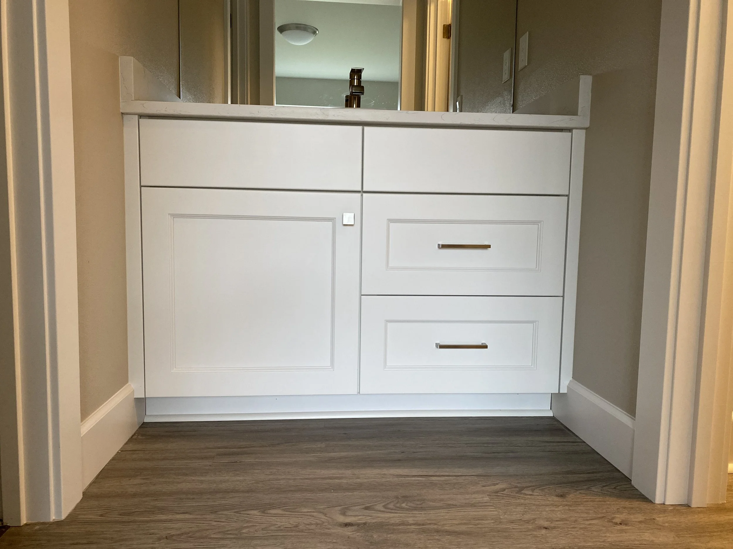 White bathroom vanity with drawers and cabinet, granite countertop, and a faucet, against a beige wall with mirror above.