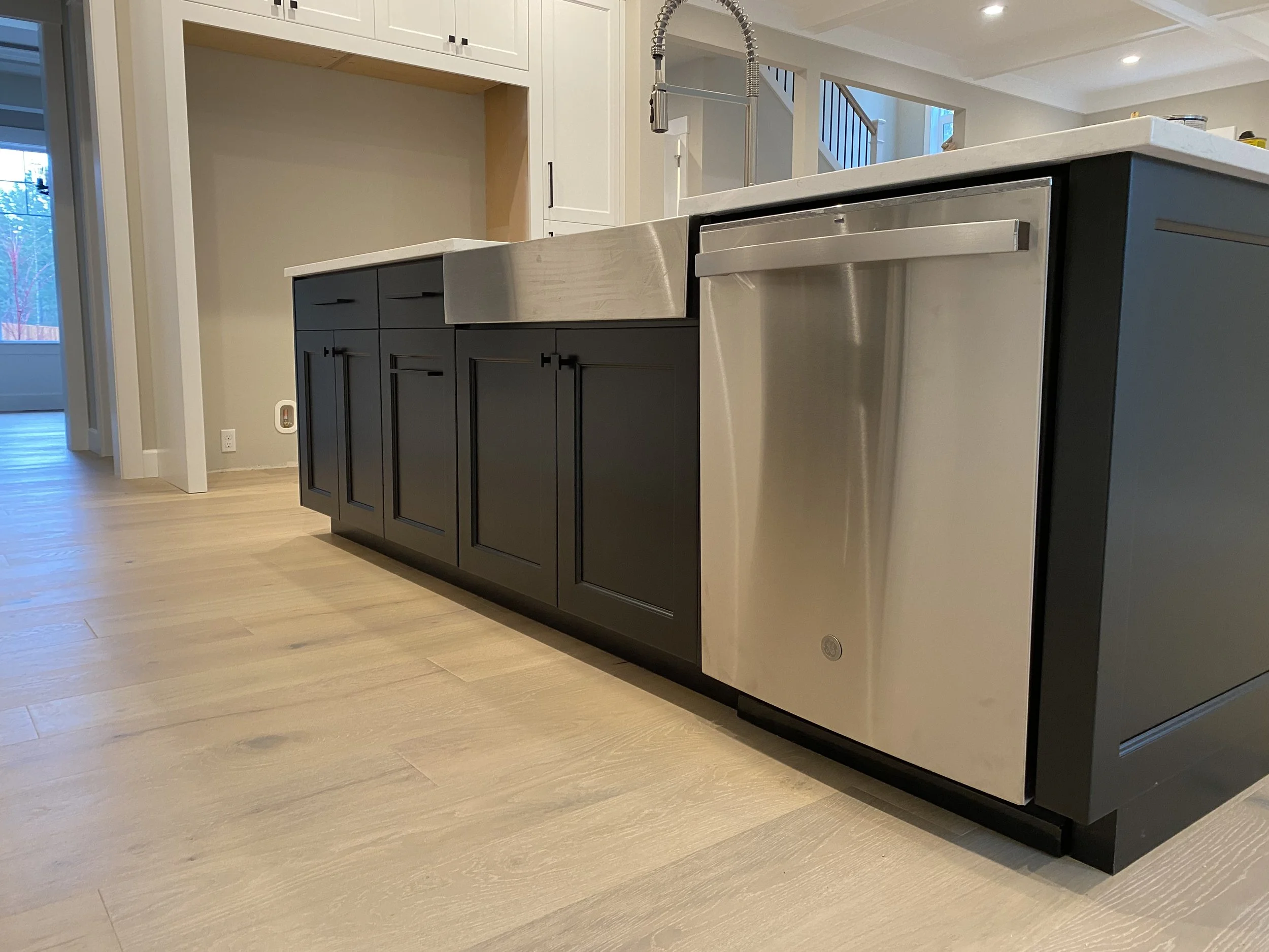 Modern kitchen island with dark cabinetry, stainless steel dishwasher, and a white countertop.