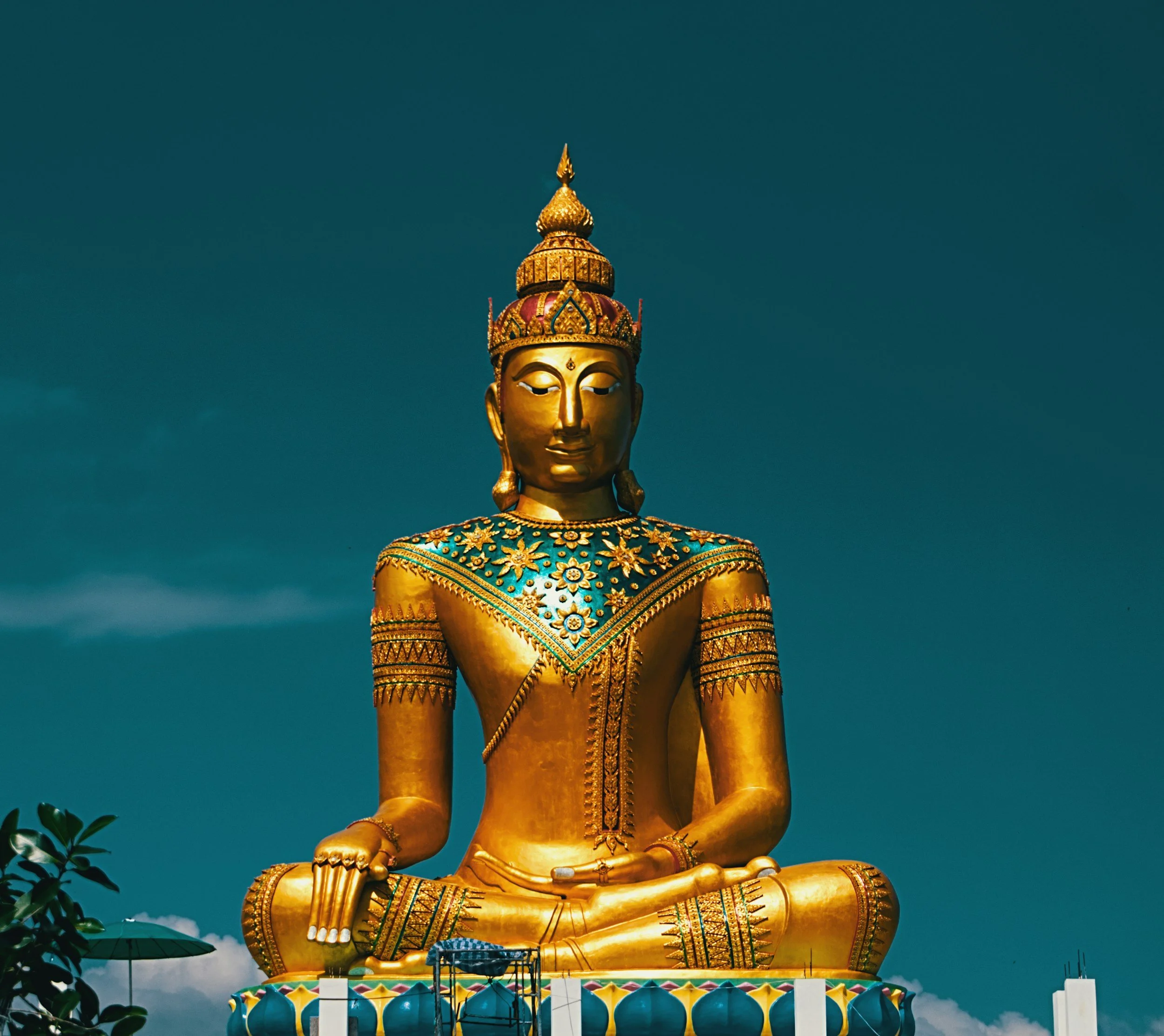 Large golden Buddha statue seated in a meditative pose against a cloudy sky.