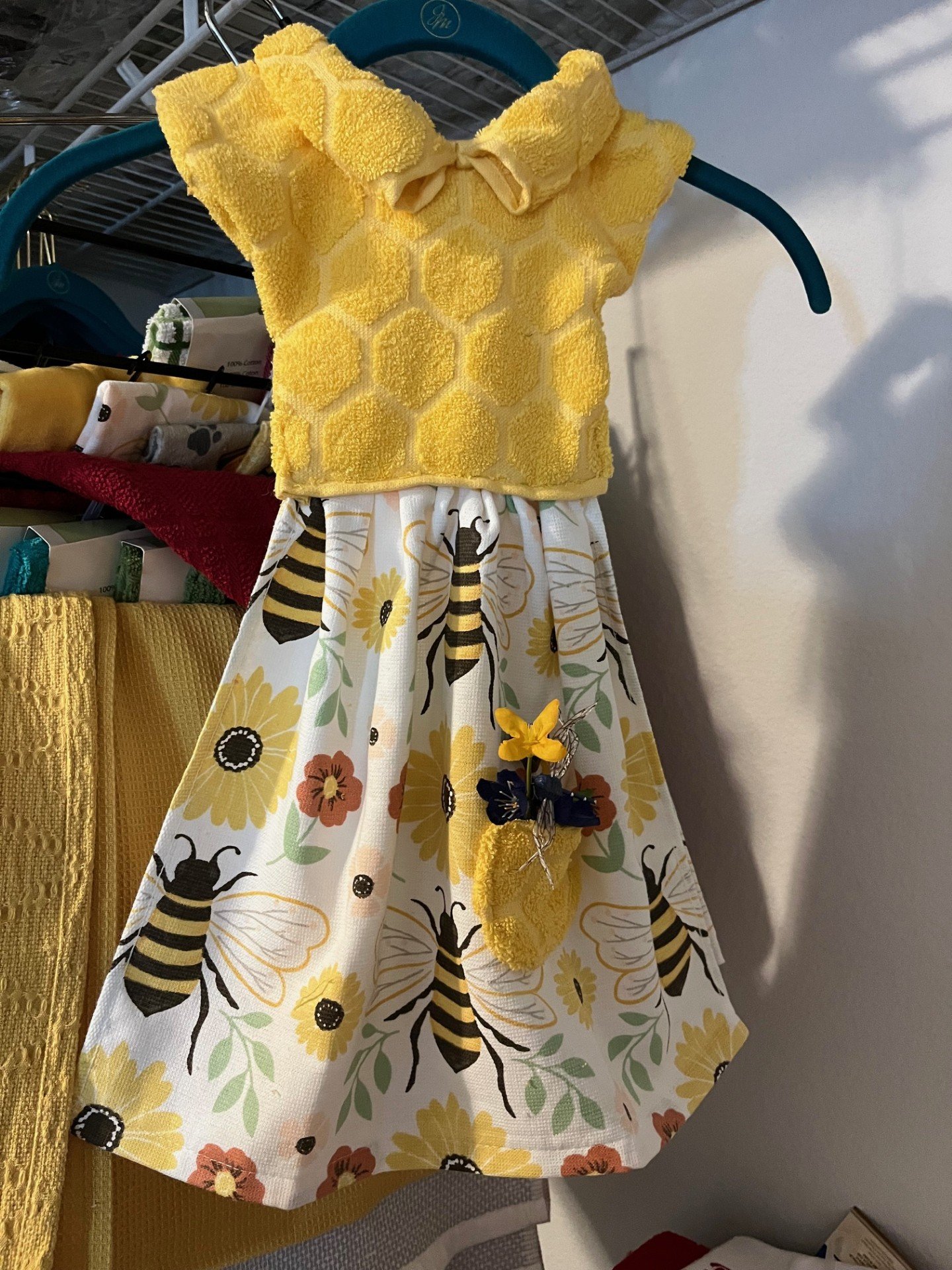 A yellow Oven Towel dress made from two Tea Towels for a hanging on the oven. The "Busy Bee" dress has a textured top with a honeycomb pattern and a floral skirt featuring bees and flowers.