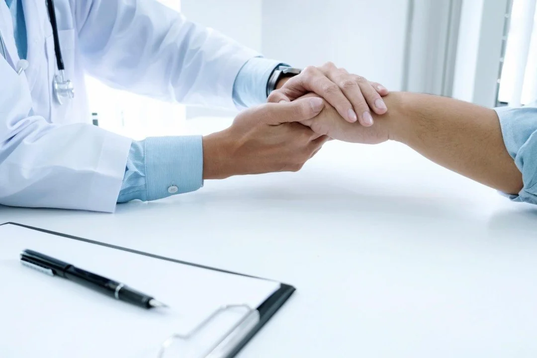 Doctor comforting a patient by holding their hand during a consultation.