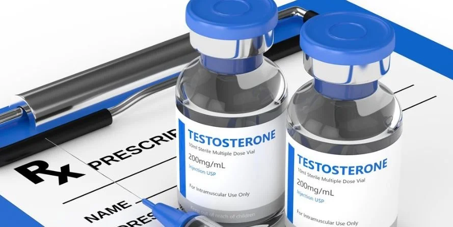 Two vials labeled testosterone with blue caps and a syringe, placed on a prescription pad with the words 'Rx Prescription' visible.