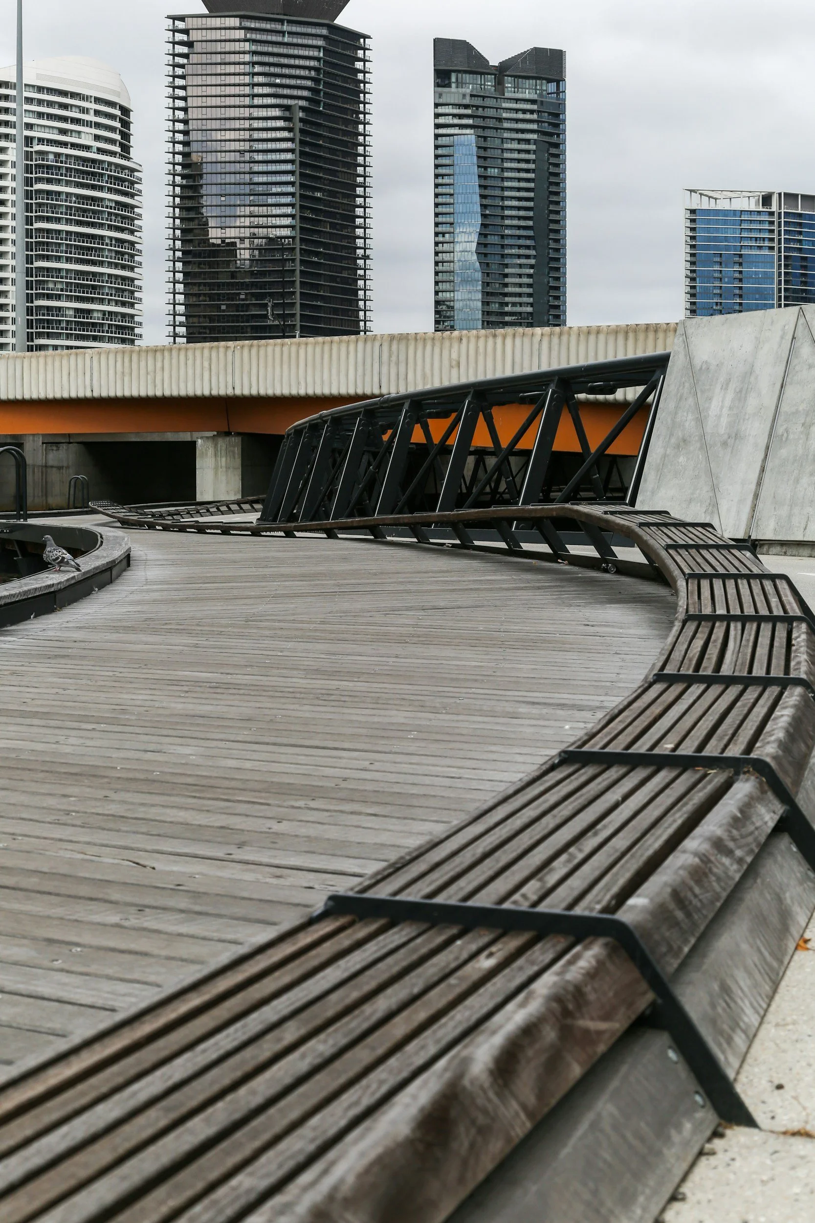 Urban scene with wooden benches, a curved walkway, and tall modern buildings in the background.