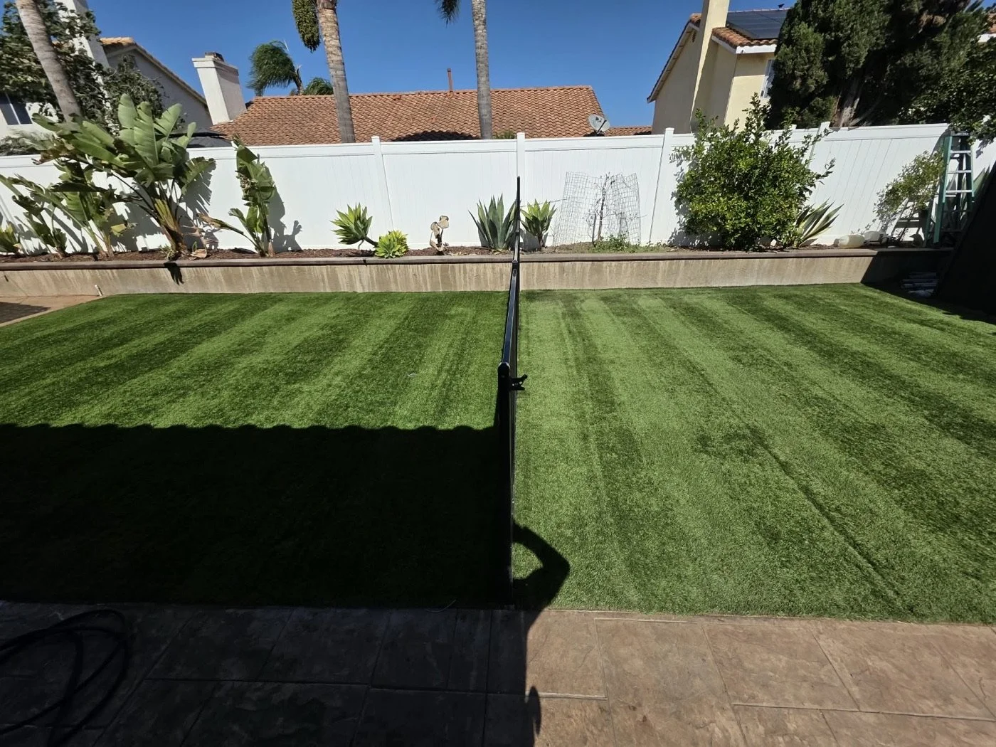 Fenced backyard artificial turf groomed into stripes after a HydroForce deep clean