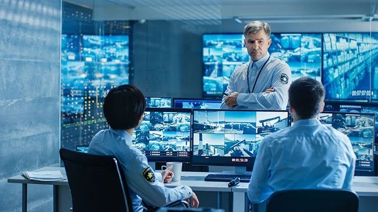 Security operations center with three professionals analyzing surveillance footage on multiple monitors.