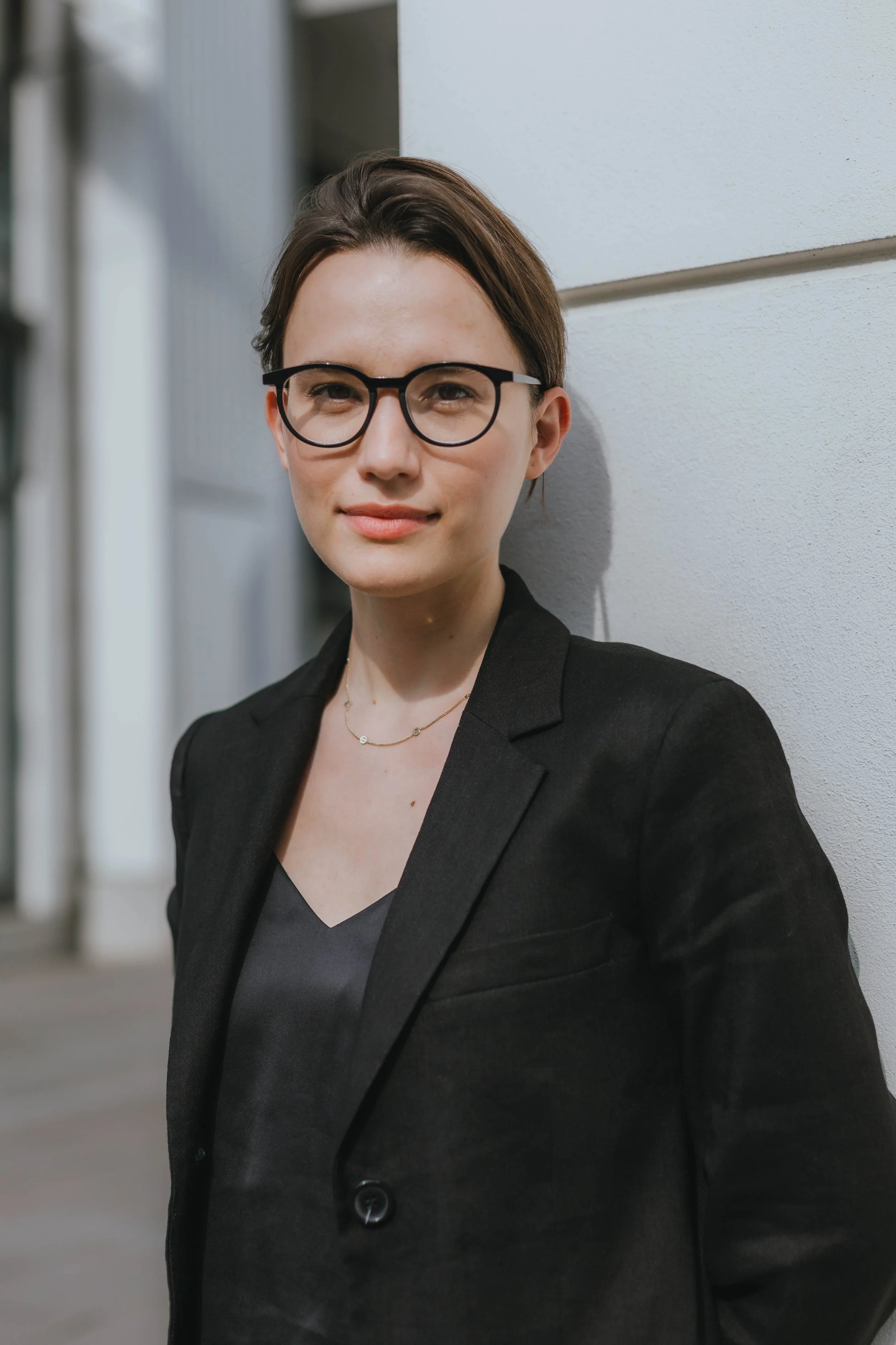 Junge Frau mit Brille in dunkler Blazer vor weißer Wand
