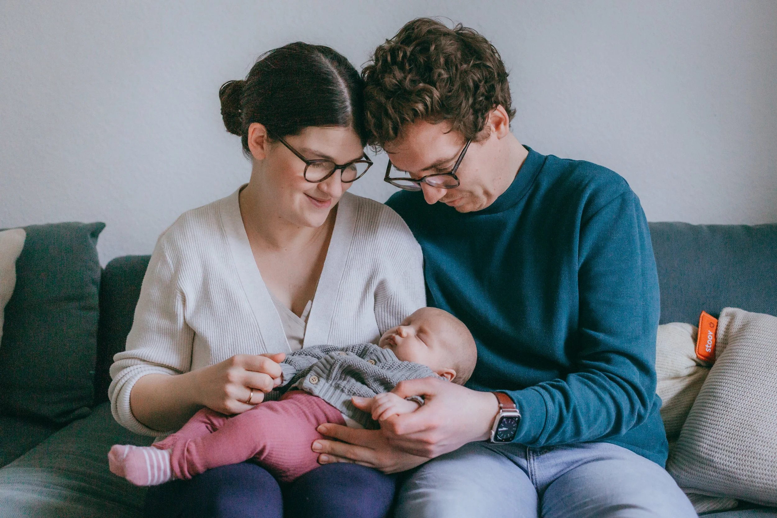 Ein glückliches Elternpaar hält ein schlafendes Baby auf dem Schoß auf einem Sofa.