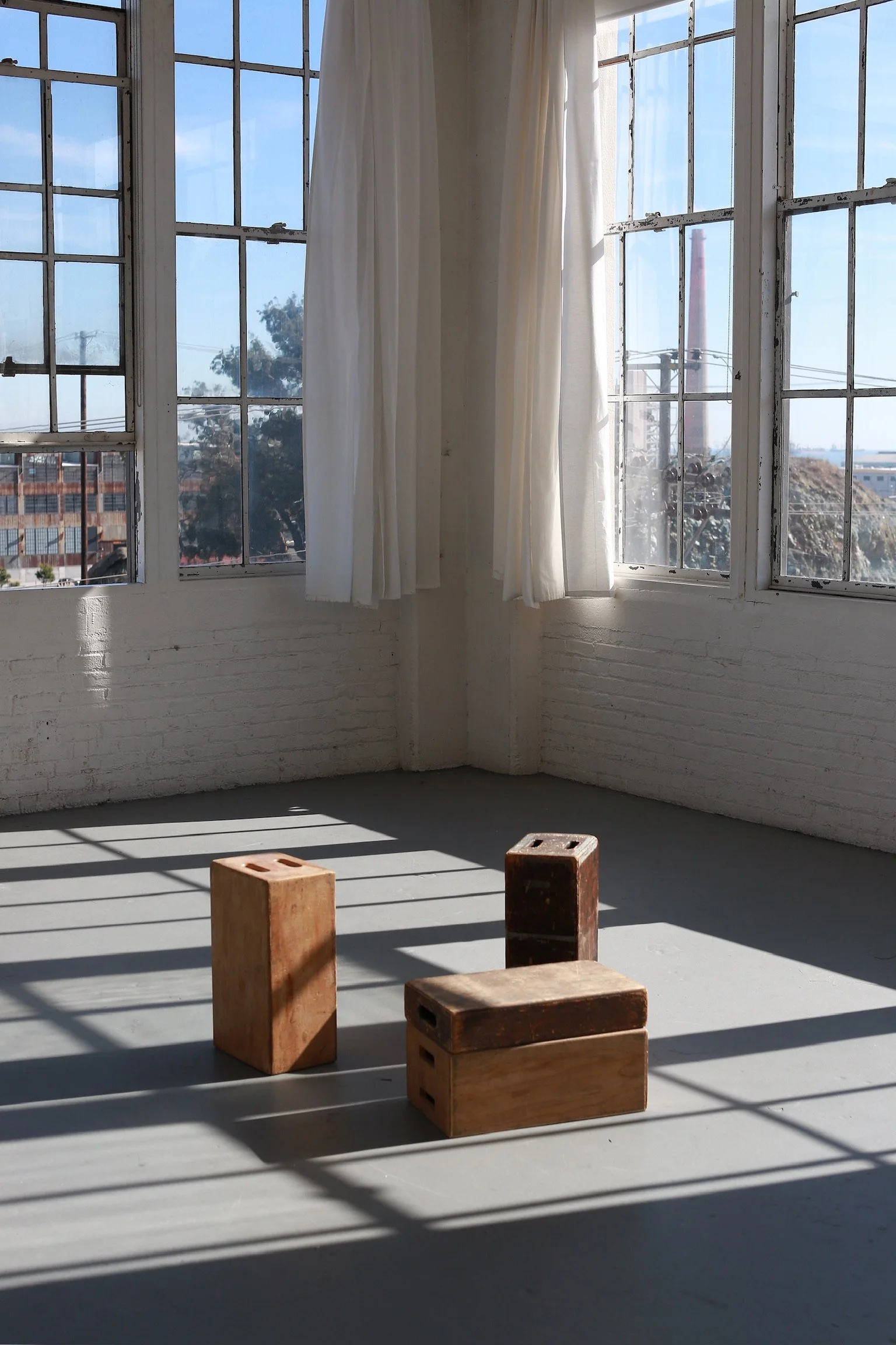 Sunlit room with large windows and white curtains, four wooden gymnastic blocks on the floor casting striped shadows.